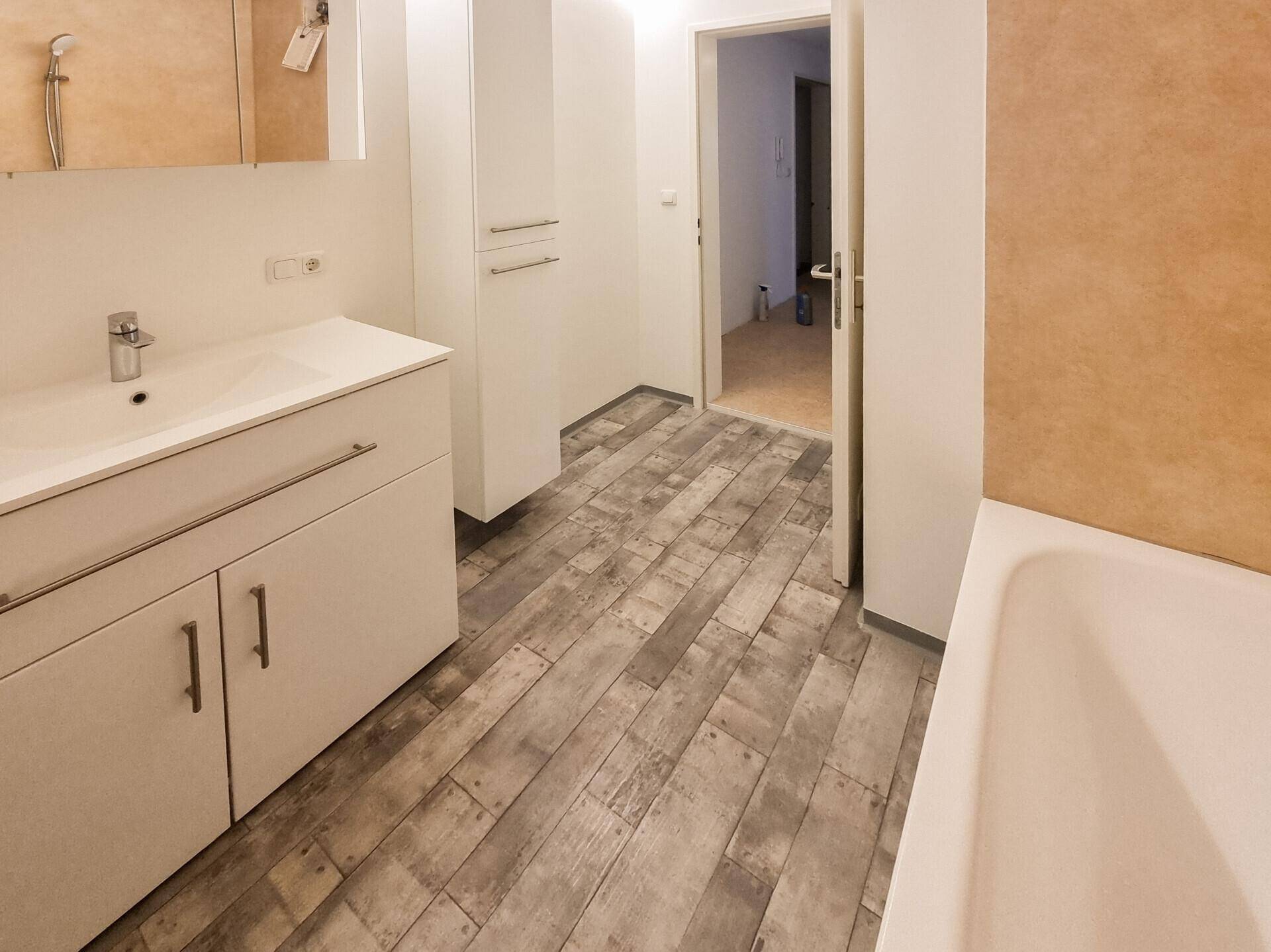 Badezimmer mit Waschtisch, Spiegelschrank und Vinylboden, Blick in den Flur.