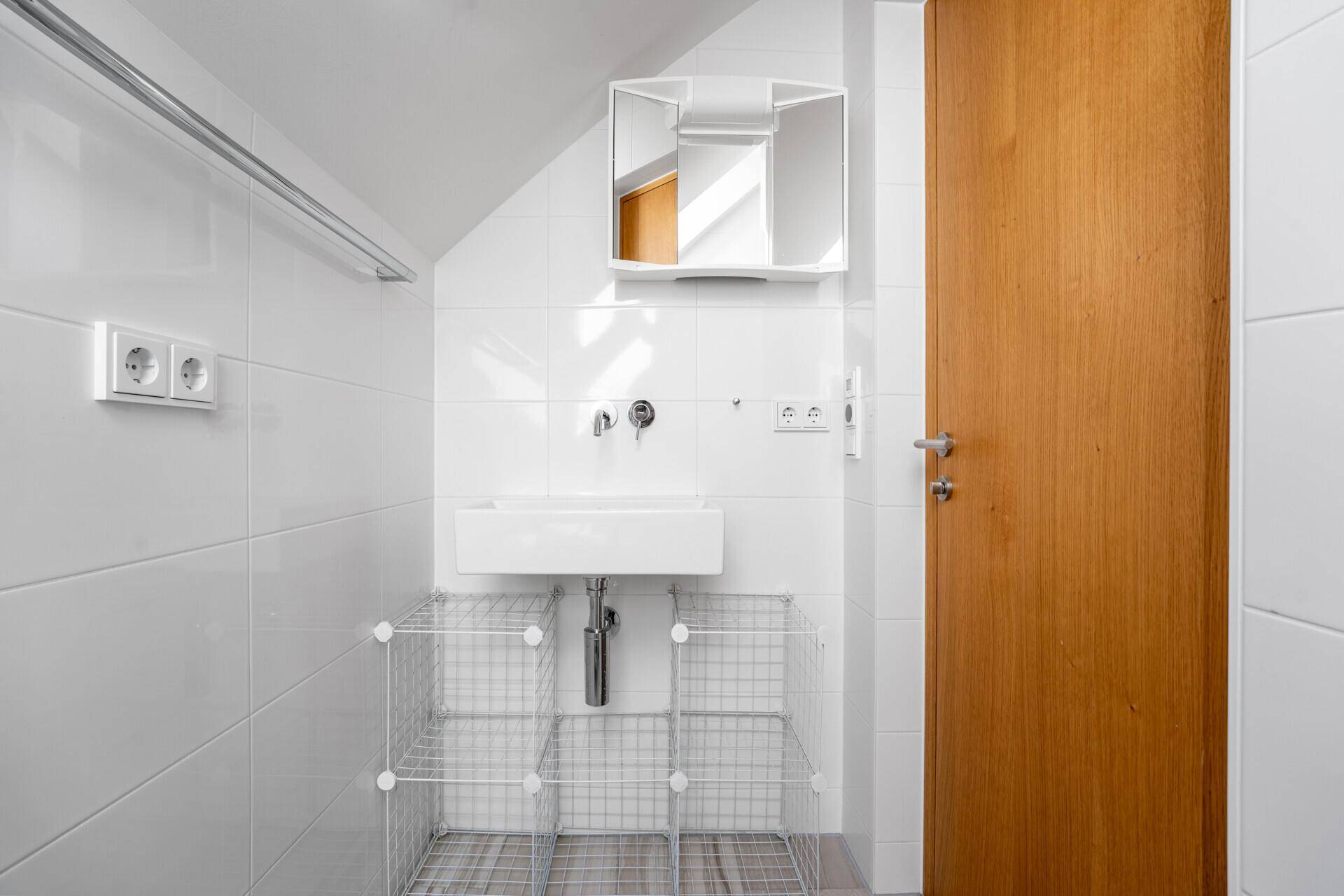 Helles Badezimmer mit weißen Fliesen, modernem Waschbecken und Spiegelschrank unter einer Dachschräge.