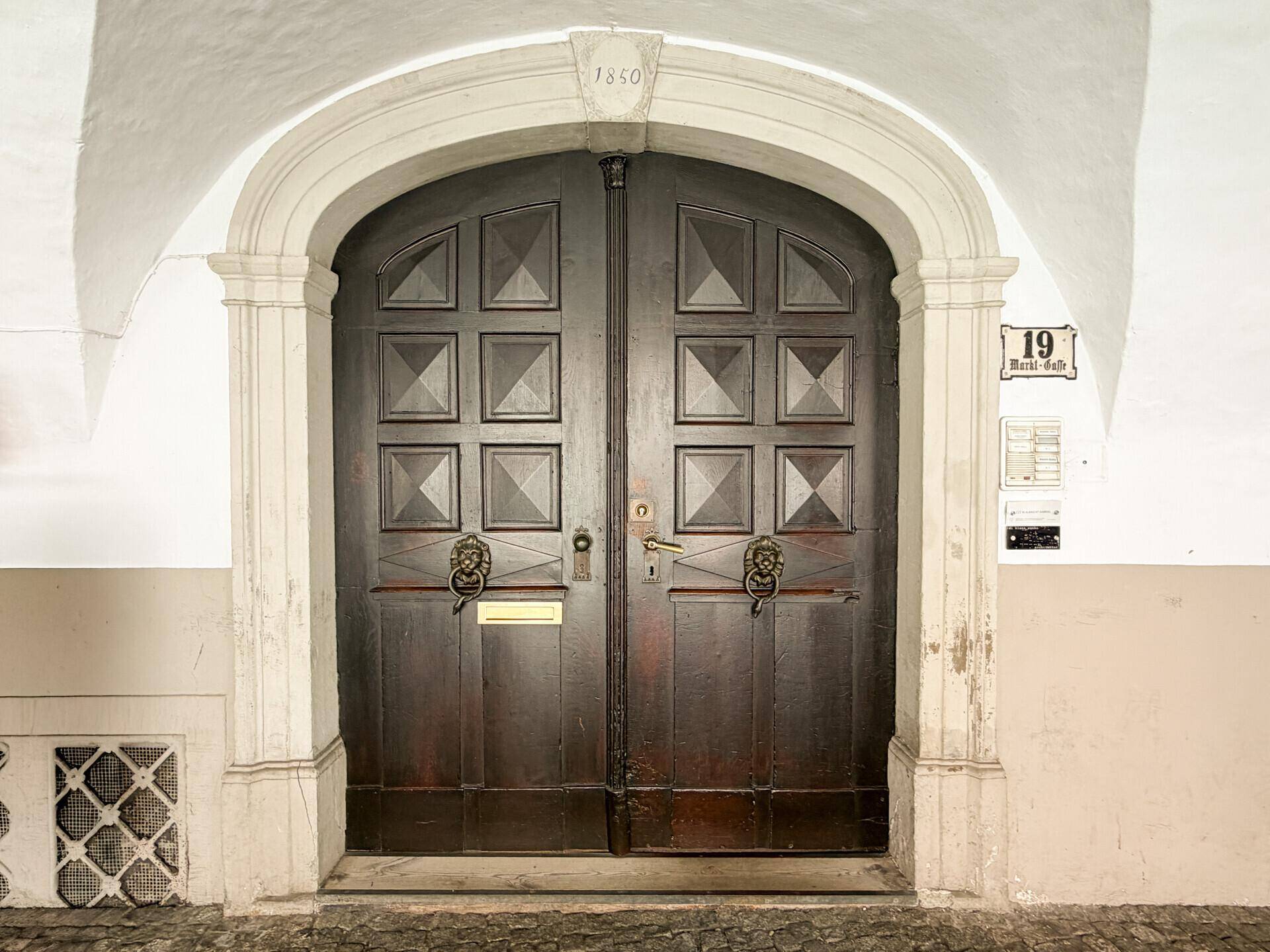 Repräsentatives Holztor mit Löwenköpfen und Jahreszahl 1850 an einem historischen Gebäude.