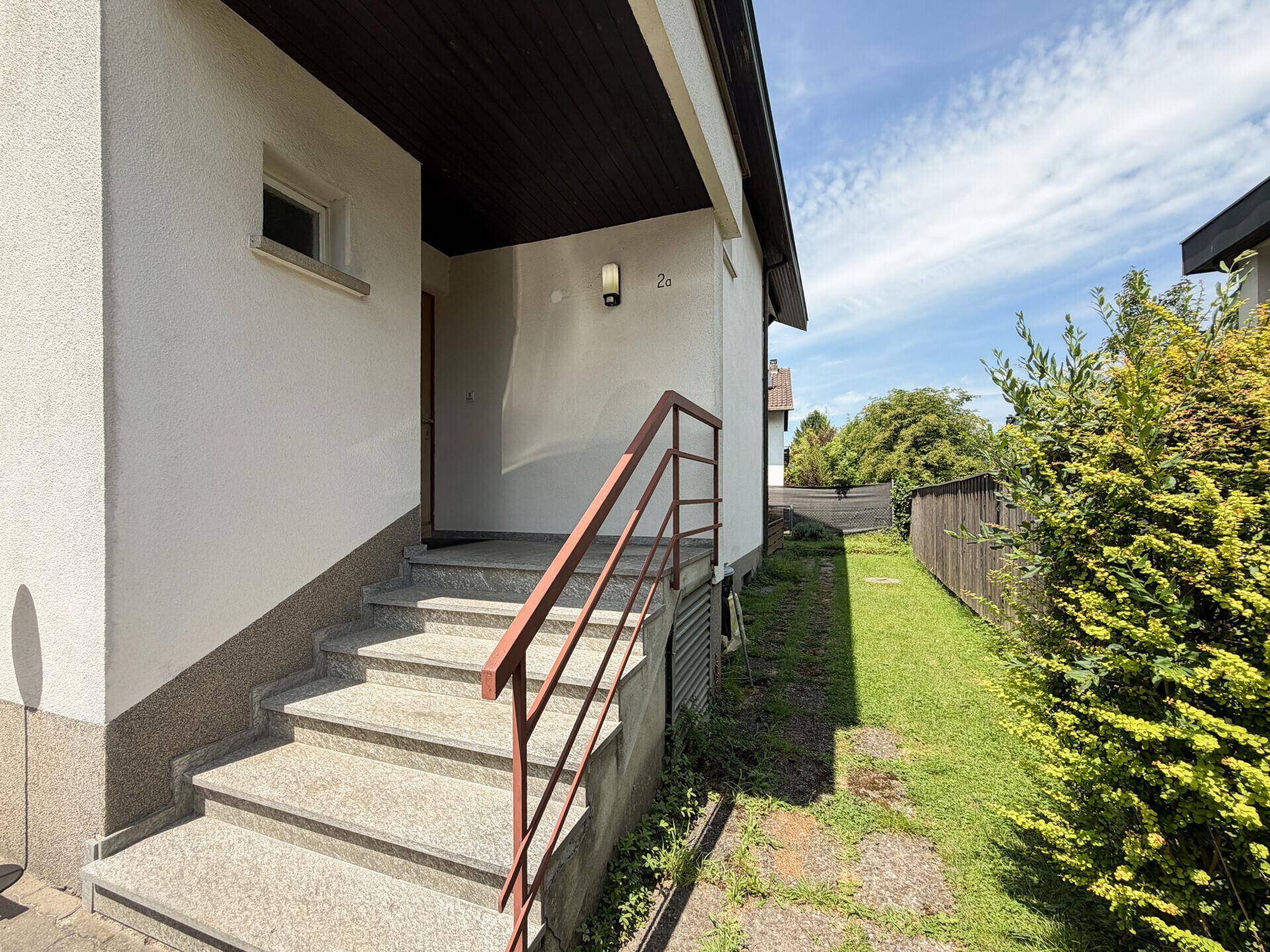 Eingangsbereich des Hauses mit Steintreppe, Metallgeländer und einer Außenleuchte.