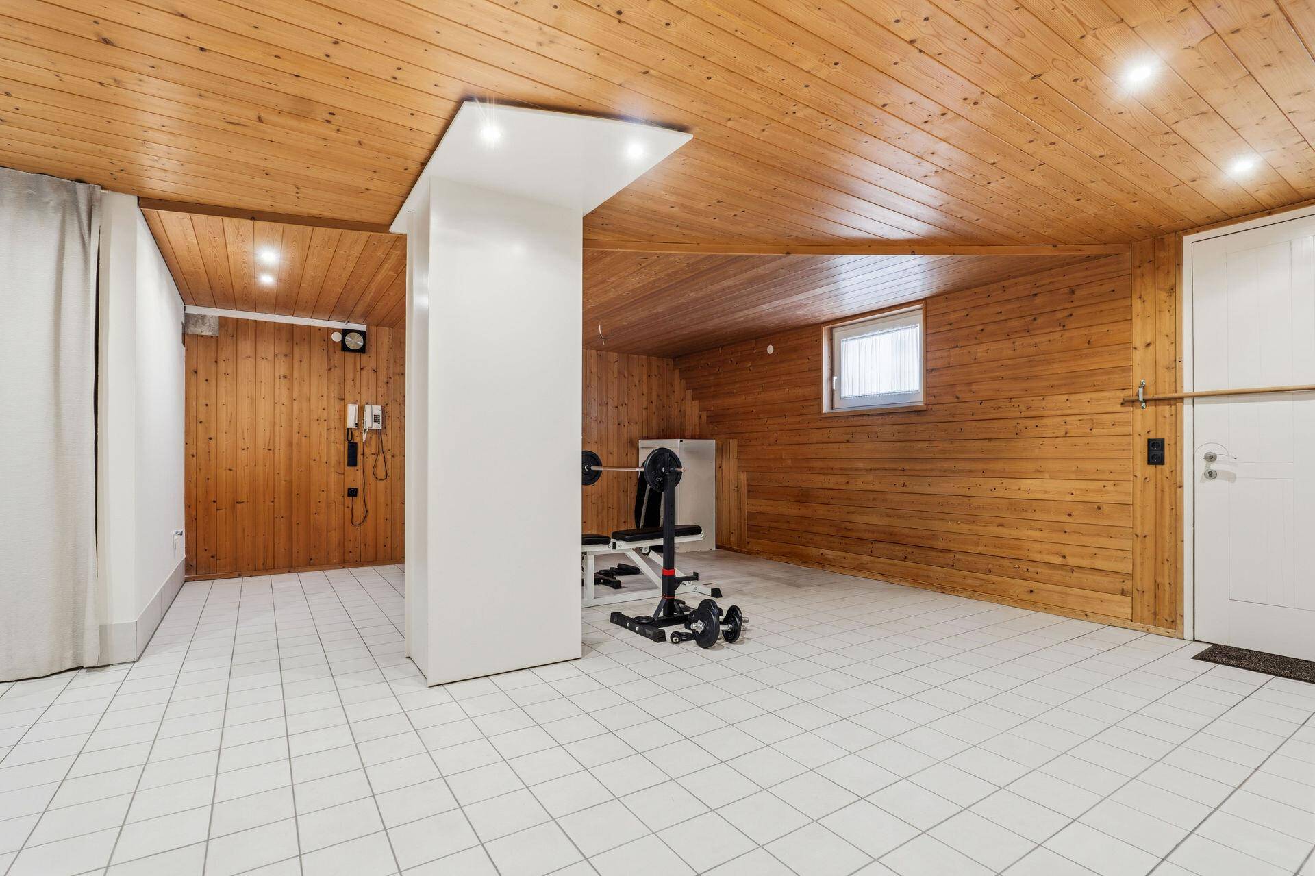 Geräumiger Fitnessraum mit Holzwänden, Fliesenboden und Trainingsgeräten.
