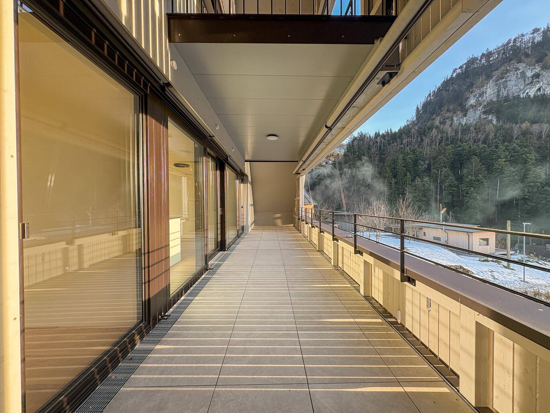 Langer Balkon mit Fliesenboden und weitem Blick auf die umliegenden Berge und Natur.