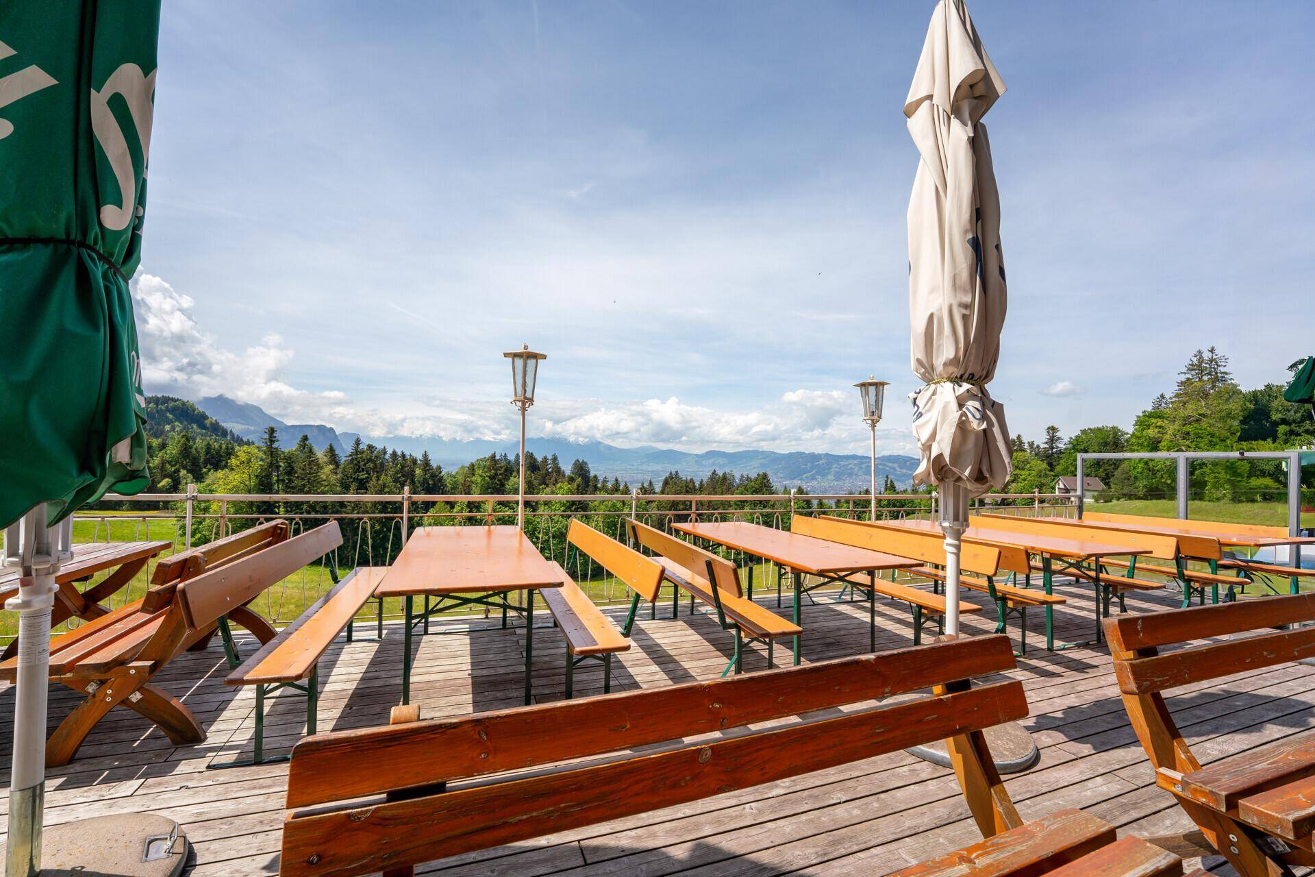 Weitläufige Holzterrasse mit zahlreichen Sitzgelegenheiten und Sonnenschirmen, bietet einen Panoramablick auf die Landschaft.