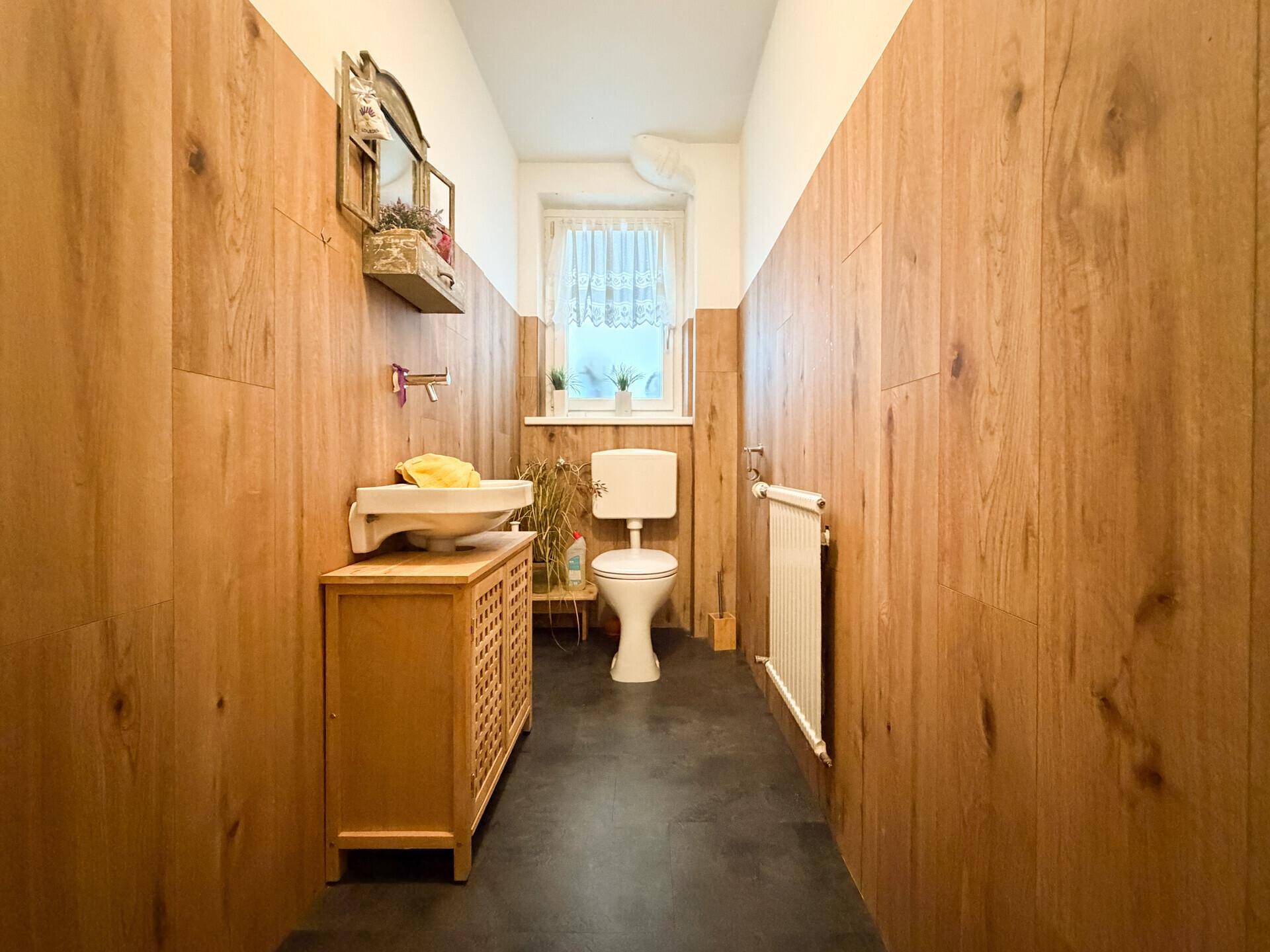 Separates WC mit Holzvertäfelung, Toilette und kleinem Waschbecken.