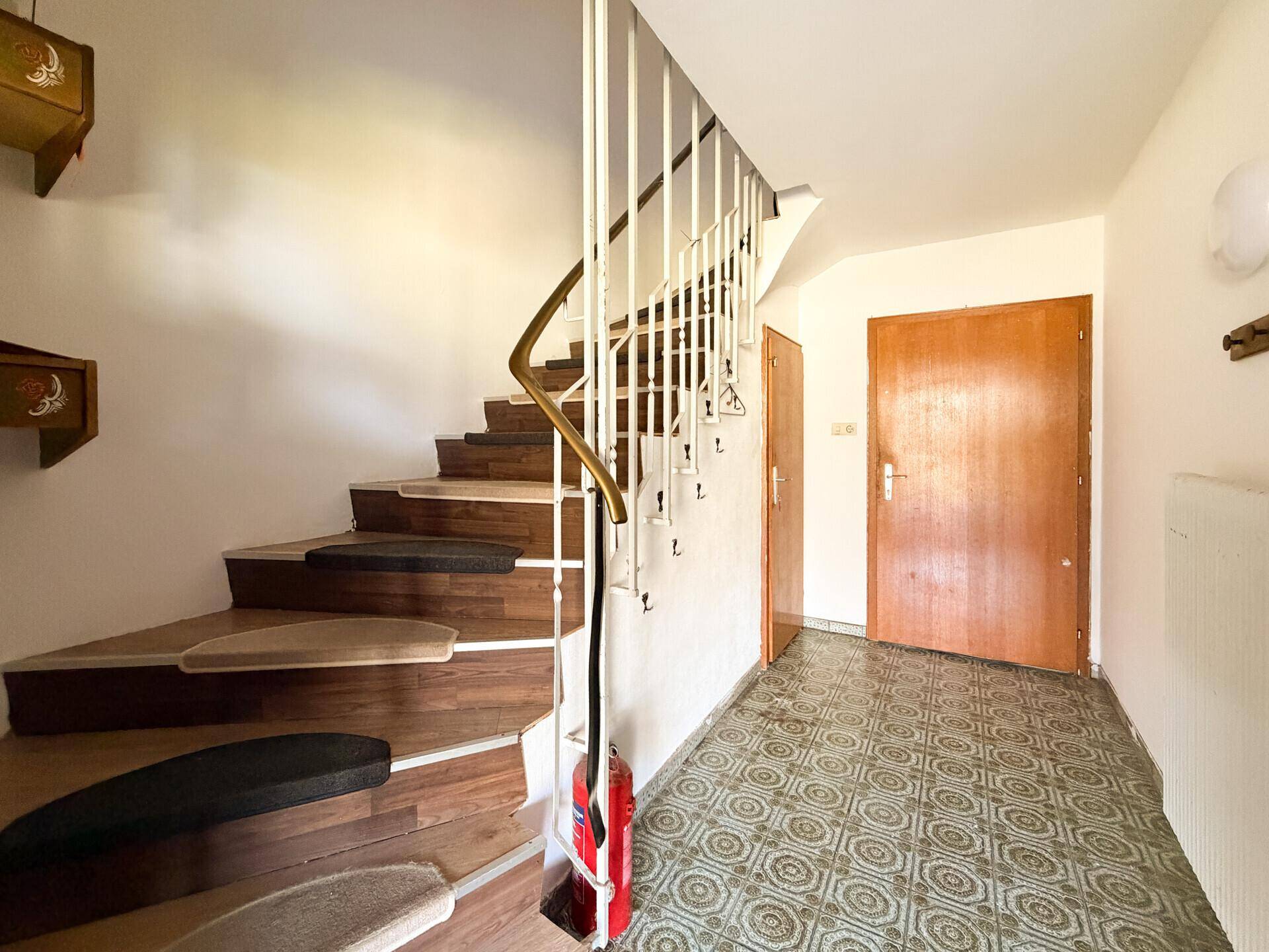 Eingangsbereich mit einer geschwungenen Treppe und gemusterten Fliesen, führt zu weiteren Räumen.