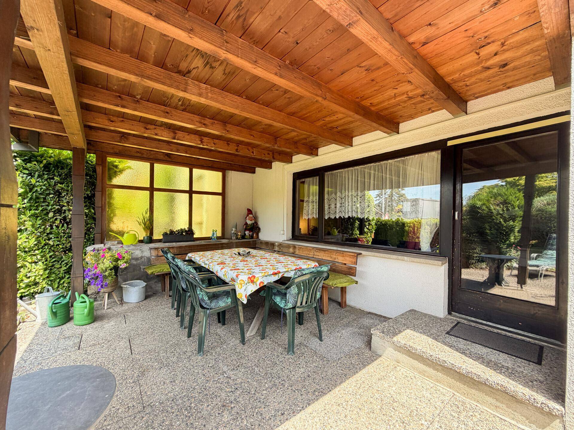 Gemütliche überdachte Terrasse mit Gartenmöbeln und Blick in den grünen Garten.
