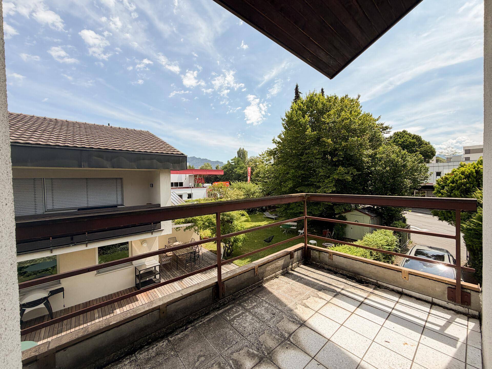 Balkon mit Fliesenboden und Holzgeländer, bietet Blick auf die grüne Umgebung und Berge.