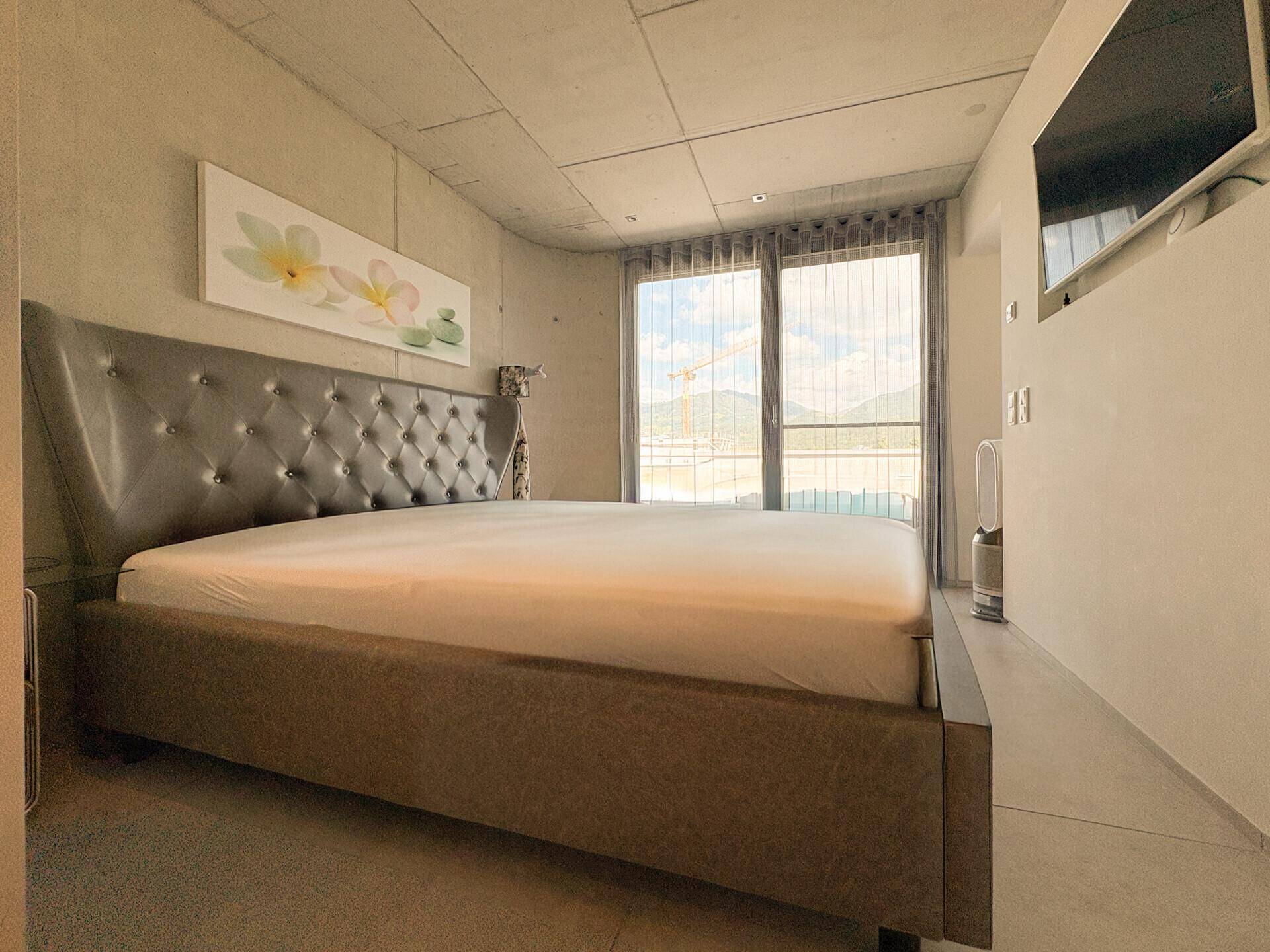 Schlafzimmer mit großem Bett, Fernseher und Zugang zu einem Außenbereich.