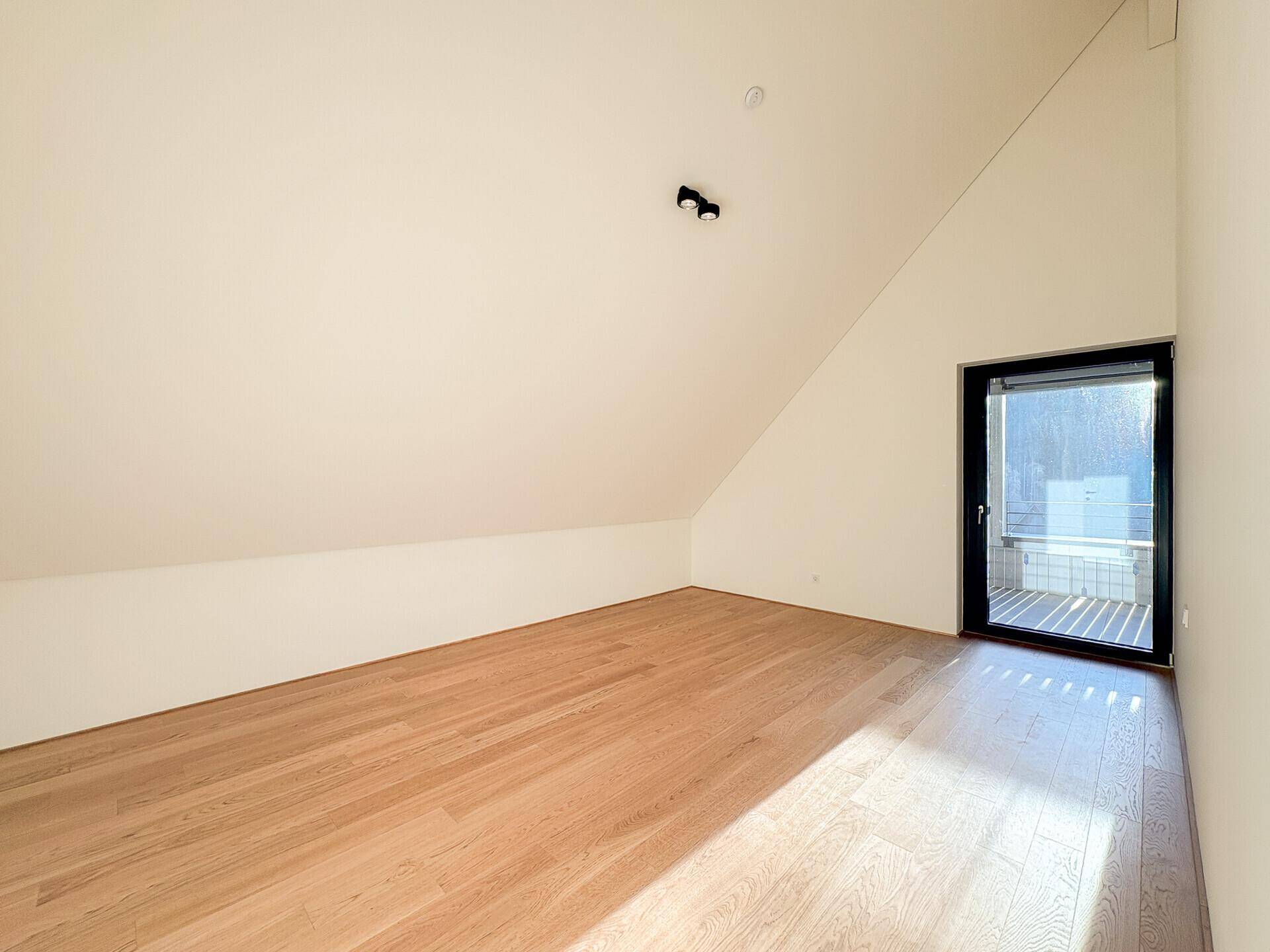 Sonniges Zimmer im Dachgeschoss mit Holzboden und Zugang zu einem französischen Balkon.