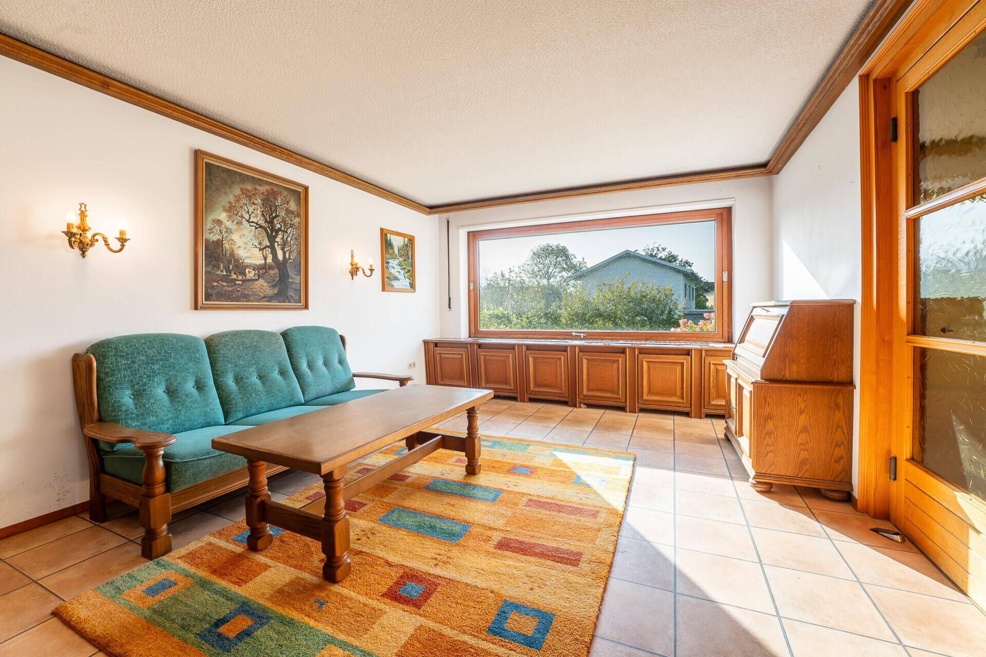 Helles Wohnzimmer mit bequemer Couch, traditionellen Holzmöbeln und großem Fenster.