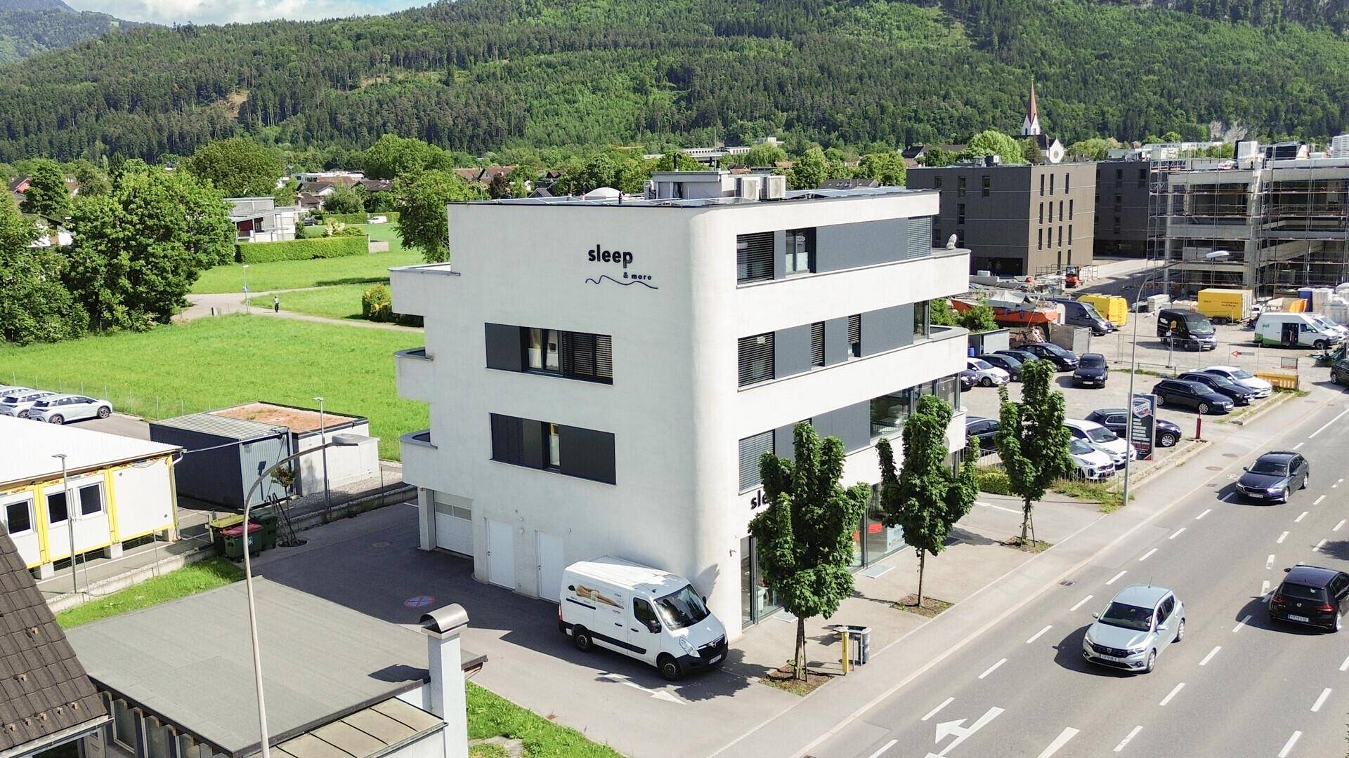 Modernes Gebäude mit minimalistischer Architektur, umgeben von Grünflächen und Parkplätzen.