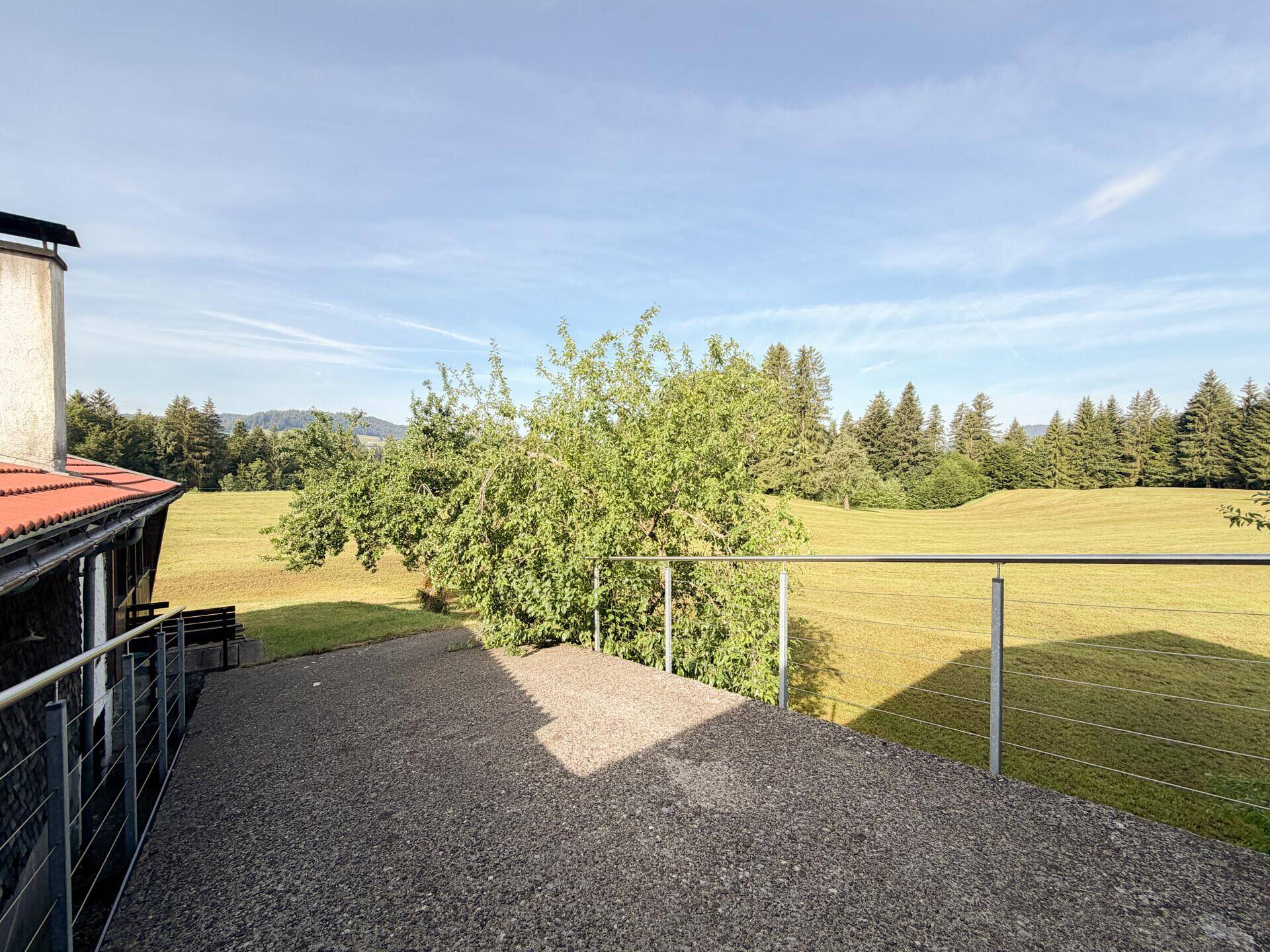 Große Terrasse mit Kiesbelag und Metallgeländer, bietet weiten Blick auf grüne Felder.
