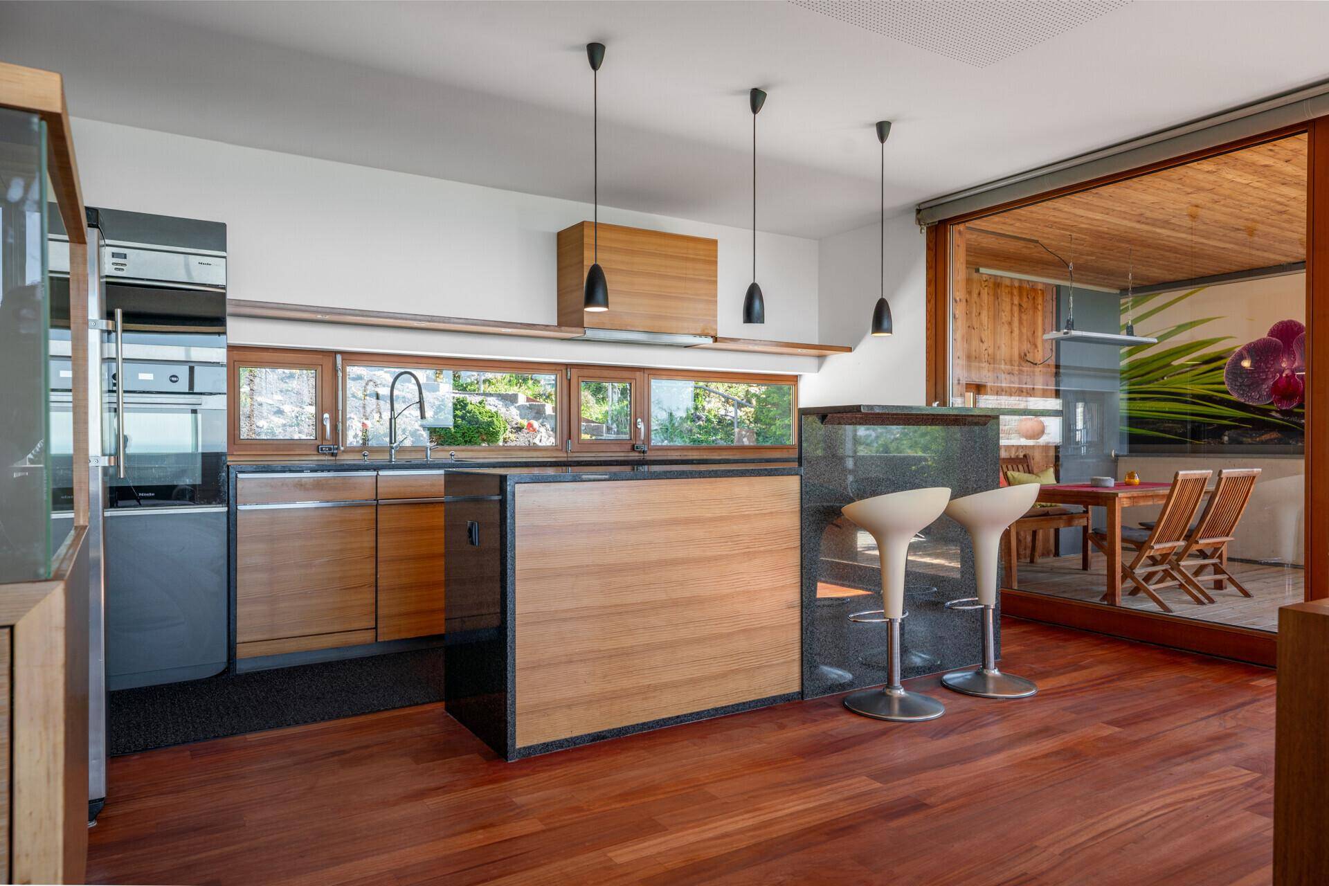 Moderne Küche mit Holzfronten, dunklen Arbeitsplatten und integrierter Frühstücksbar.