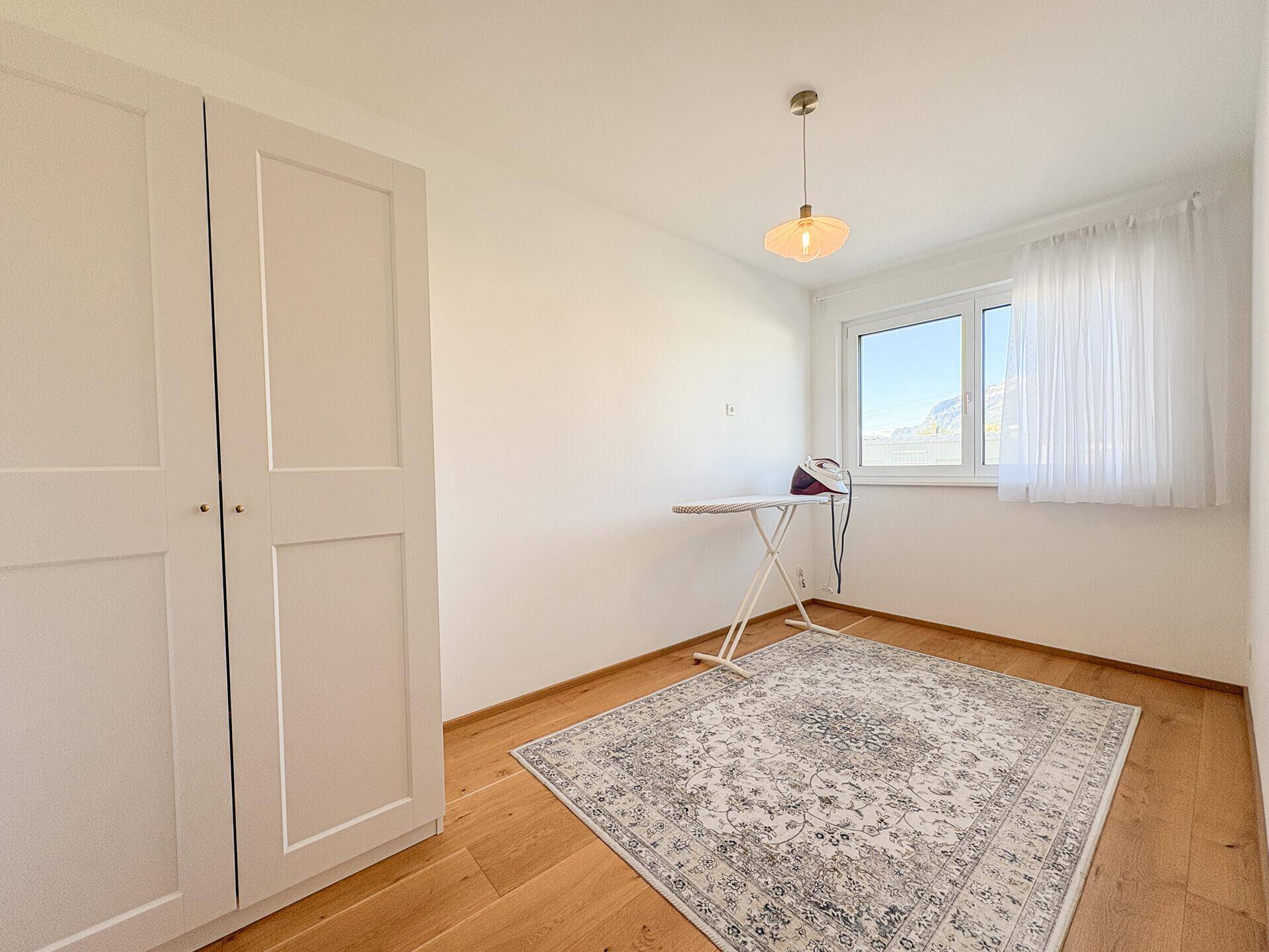 Helles Zimmer mit Holzboden, weißem Kleiderschrank und Fenster mit Bergblick.