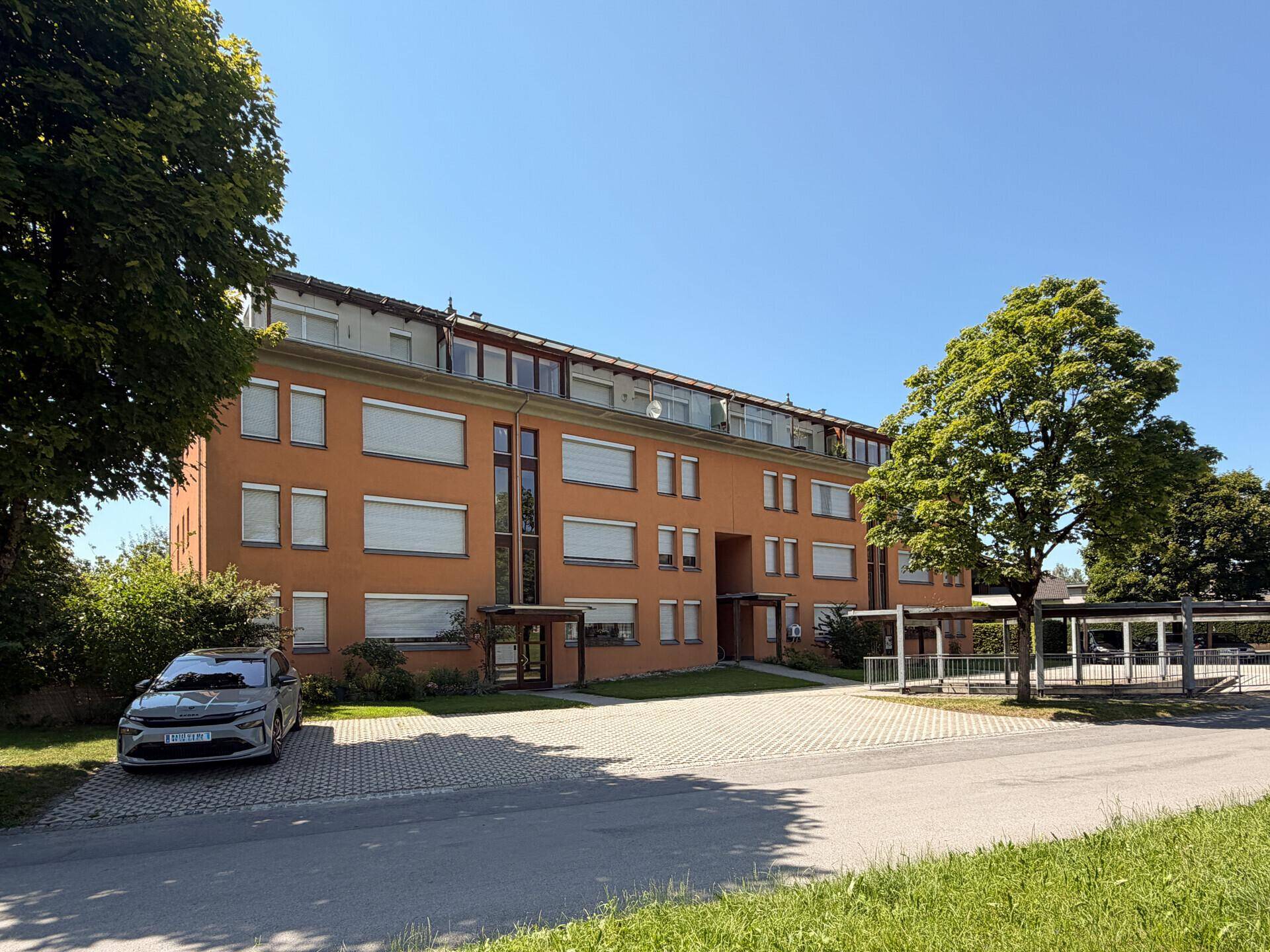 Mehrfamilienhaus mit oranger Fassade, vielen Fenstern und gepflegter Außenanlage.