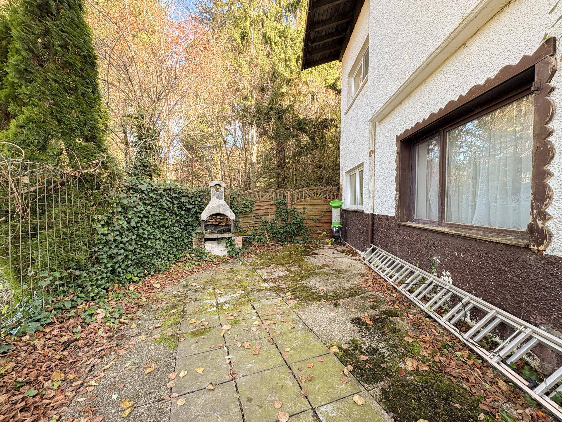 Gartenbereich mit Grillplatz, gepflastertem Weg und üppiger Vegetation.