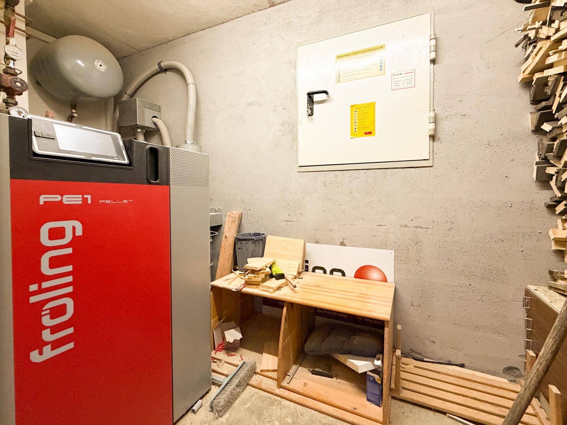 Heizraum mit moderner Pelletheizung von Fröling und Lagerung für Holzpellets an der Wand.