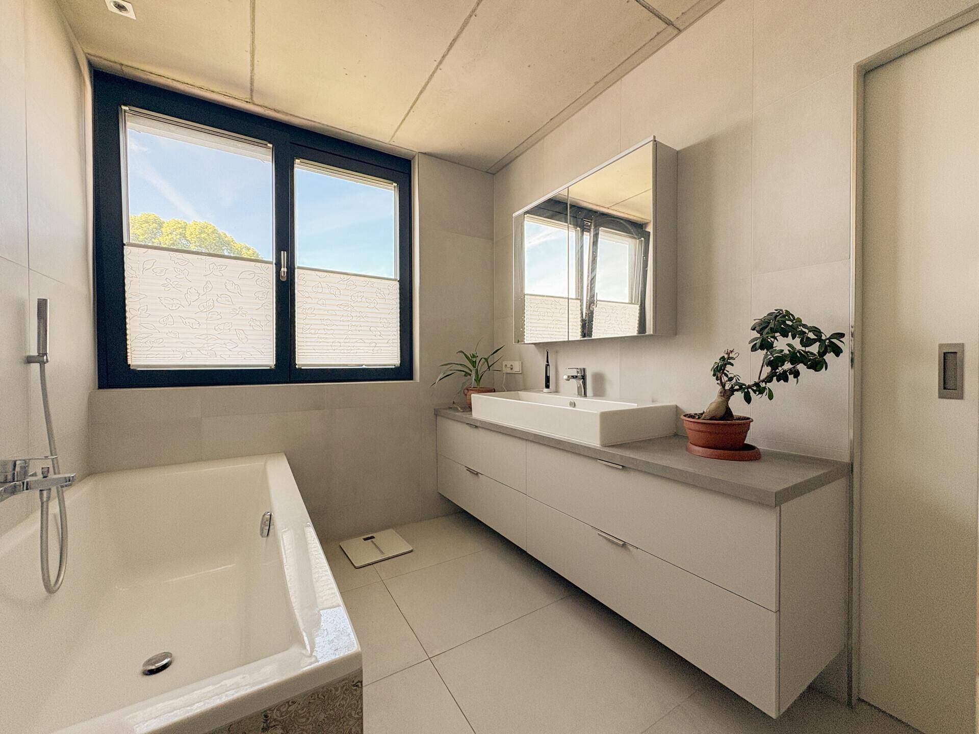 Helles Badezimmer mit Badewanne, modernem Waschtisch und großem Fenster für viel Tageslicht.