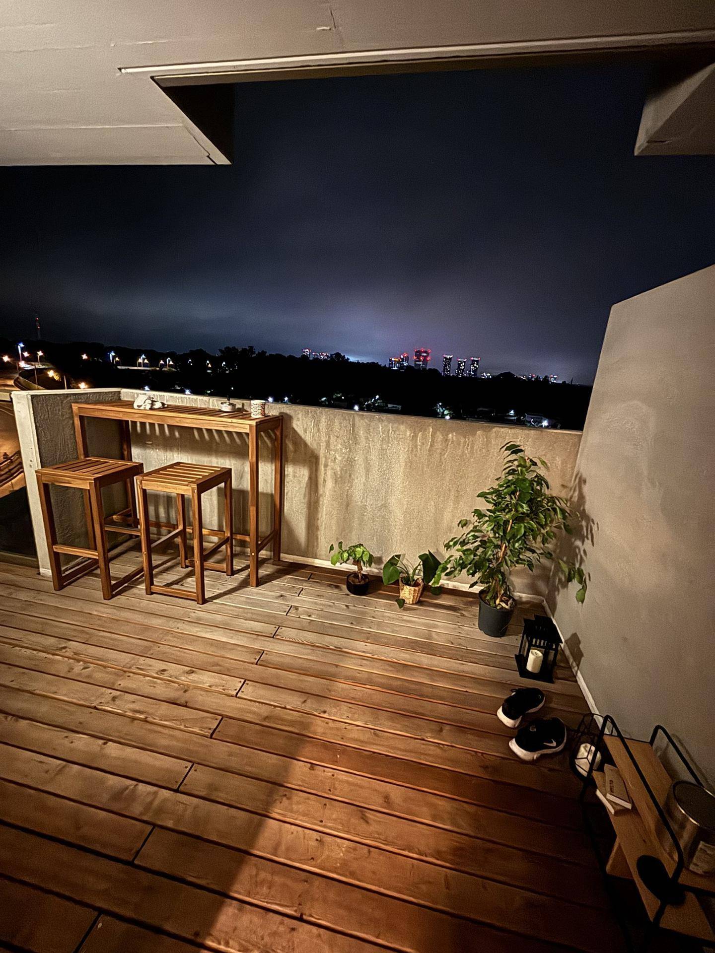 Balkon bei Nacht mit Holzboden, Bartisch und Pflanzen, bietet eine ruhige Atmosphäre.