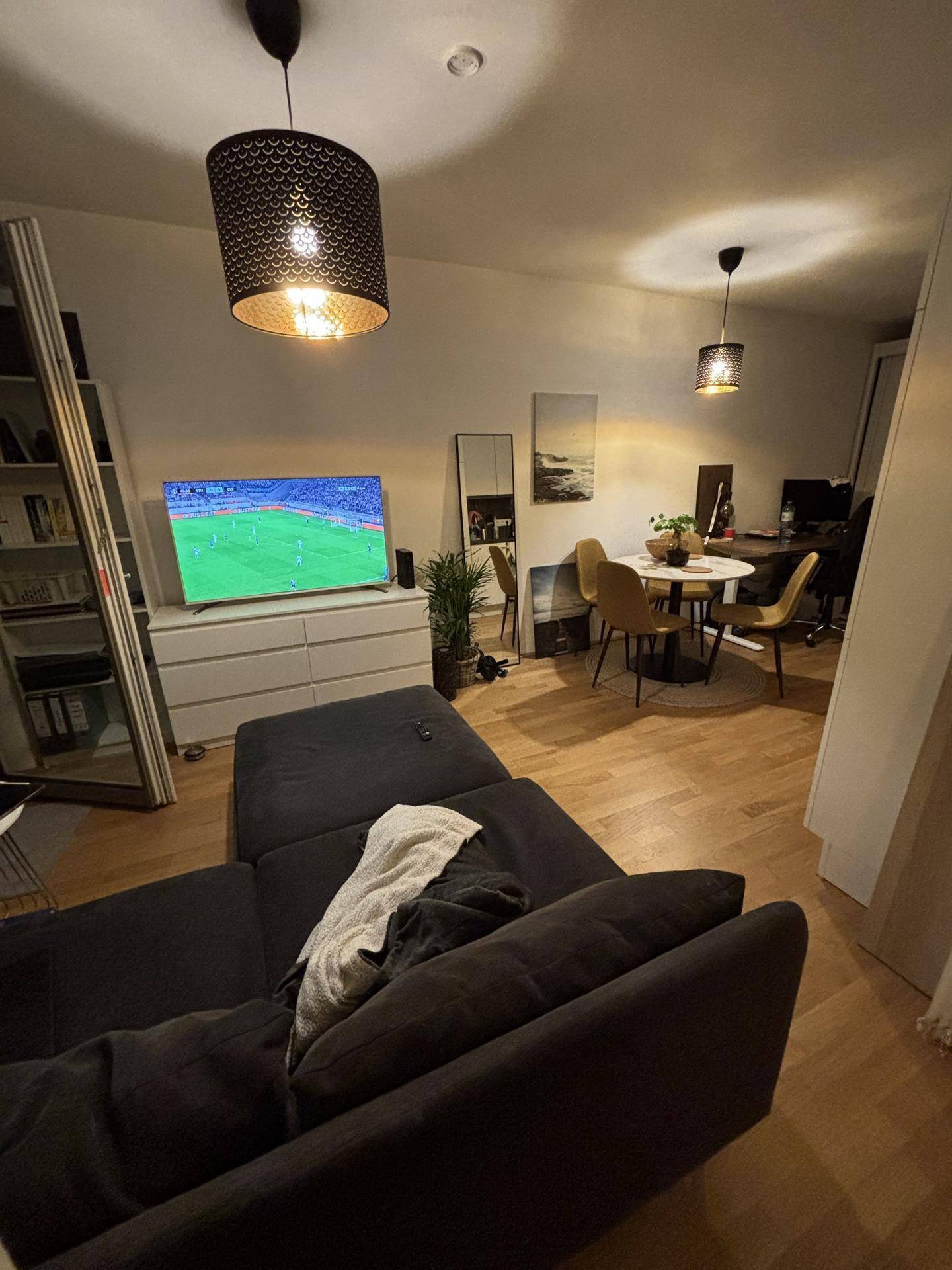 Gemütlicher Wohn- und Essbereich mit dunklem Sofa, Fernseher und einem kleinen Esstisch.