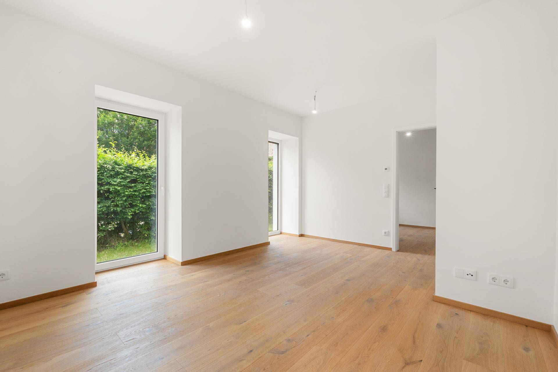 Geräumiges Zimmer mit Holzboden und großen Fenstern, die viel Tageslicht hereinlassen.
