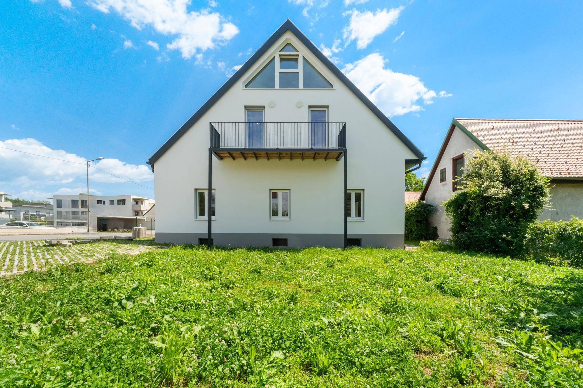 Rückansicht des Hauses mit Balkon und weitläufiger Rasenfläche im Garten.