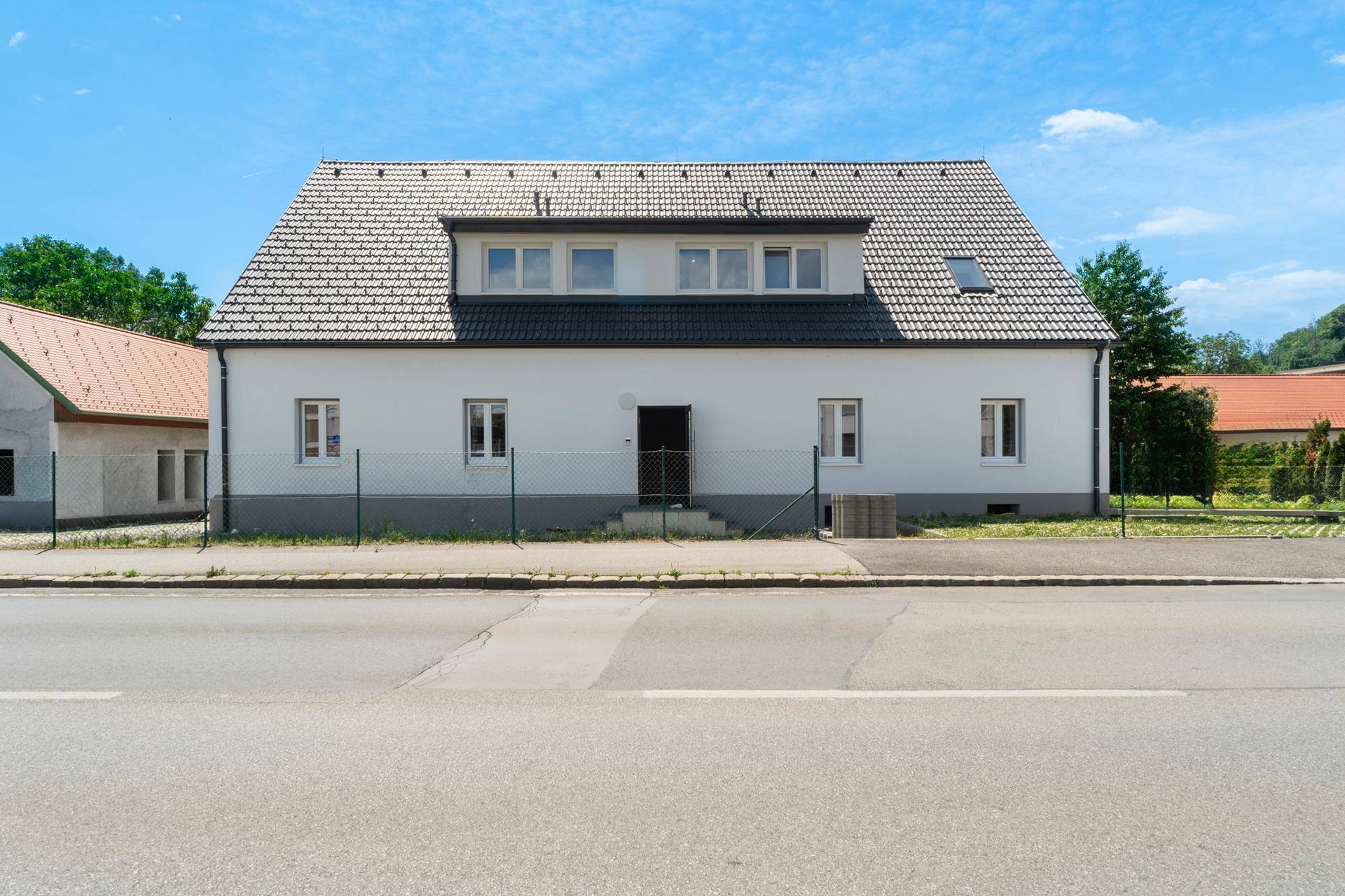 Vorderansicht des Hauses von der Straße, mit Eingangstür und mehreren Fenstern.