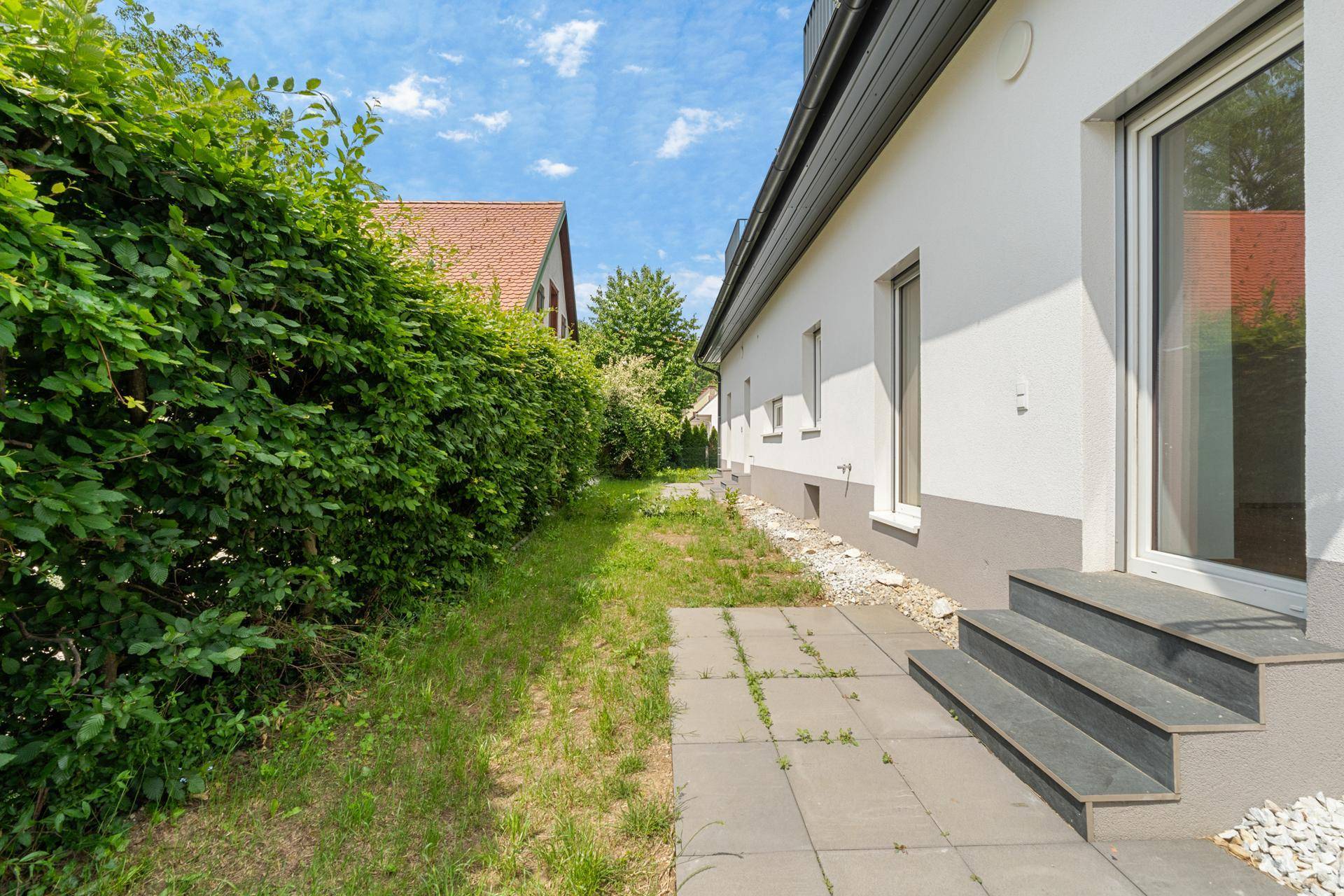 Seitlicher Gartenbereich mit gepflasterter Terrasse und grüner Hecke am Haus.
