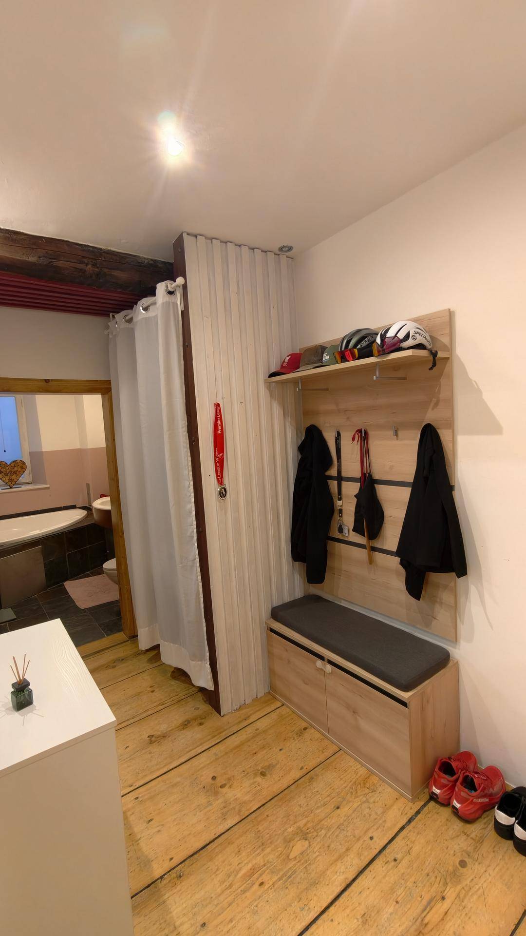 Flur mit Garderobe, Sitzbank und Holzboden, der zu einem Badezimmer führt.