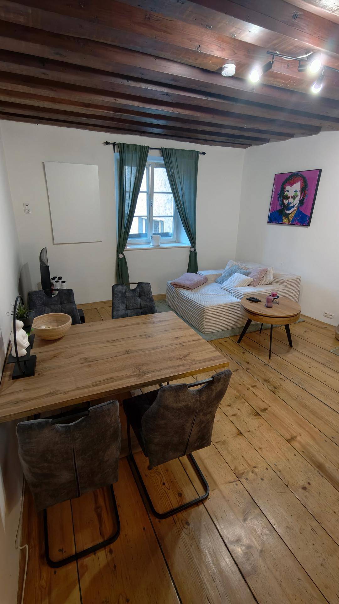 Wohn- und Essbereich mit Holzbalken, Holzboden und einem gemütlichen Sofa am Fenster.