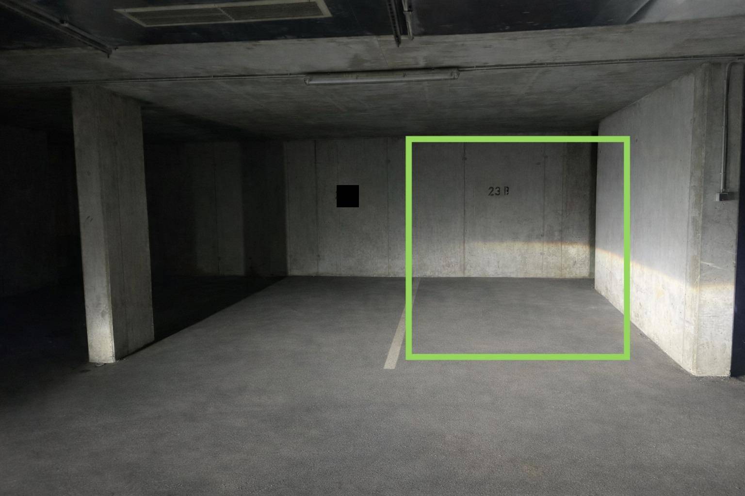 Geräumiger Tiefgaragenstellplatz mit robusten Betonwänden und -boden, beleuchtet von Leuchtstoffröhren.