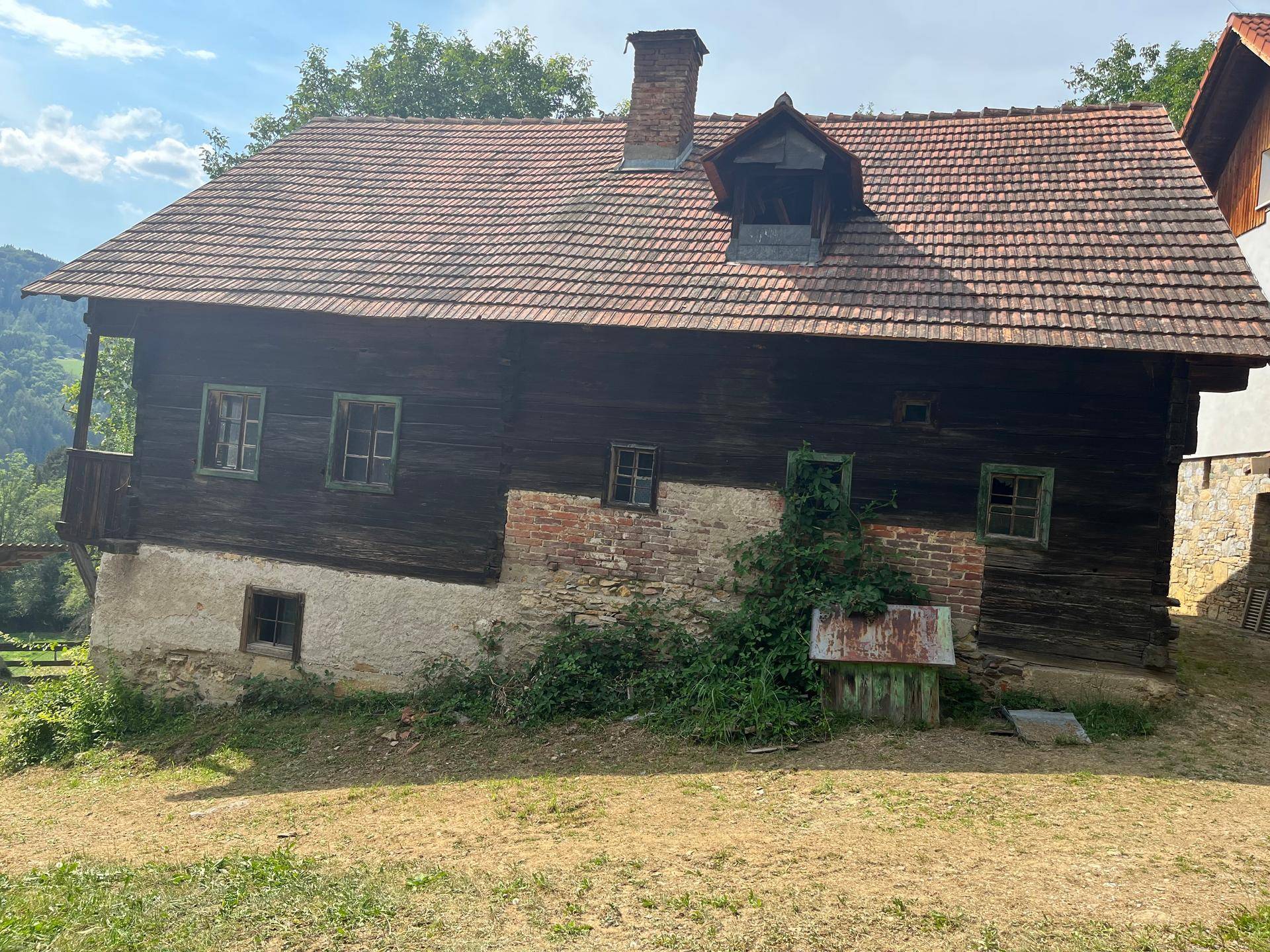 Altes Holzhaus mit Ziegeldach und grüner Umgebung, eingebettet in die Natur.