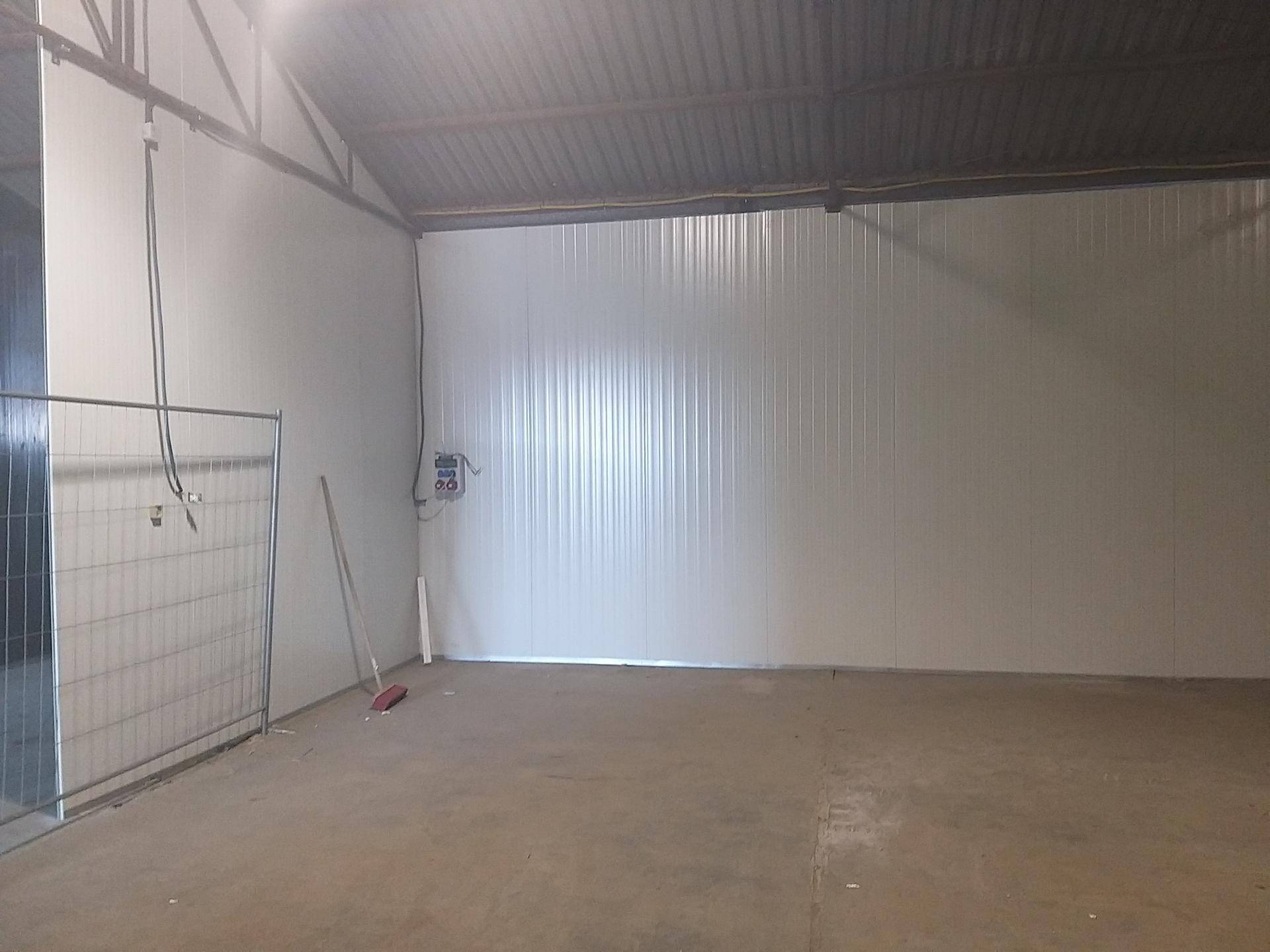 Leerer Lagerraum mit Betonboden, hoher Decke und einer temporären Metallabtrennung im Vordergrund.