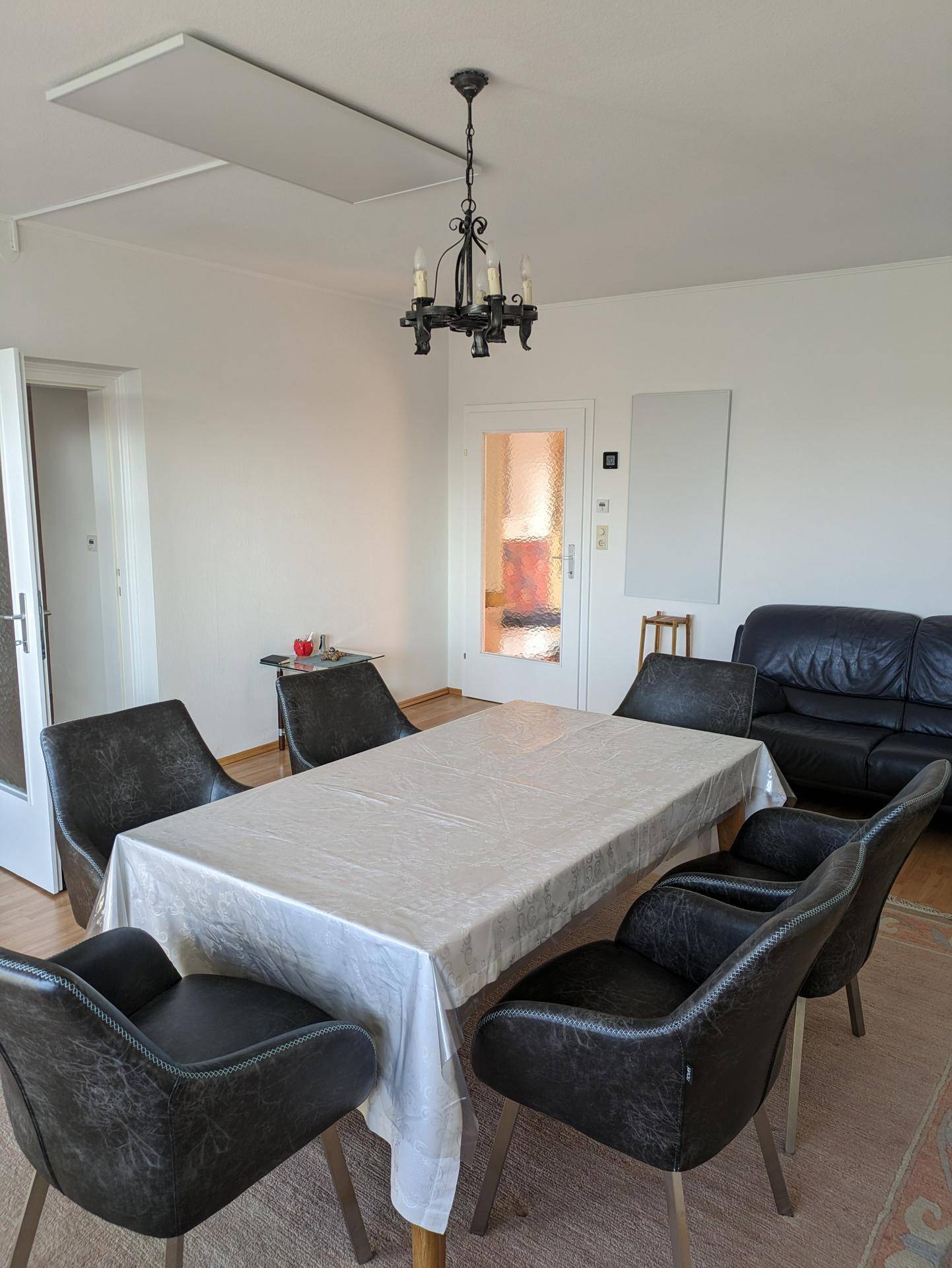 Heller Wohn-Essbereich mit großem Esstisch, bequemen Stühlen und Infrarotheizpaneelen an der Decke.