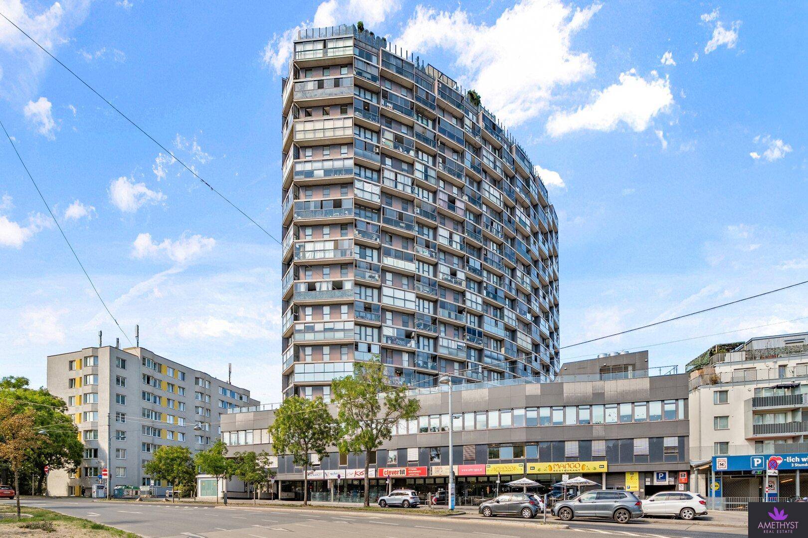 Modernes Hochhaus mit Glasfassade und Balkonen in urbaner Umgebung.