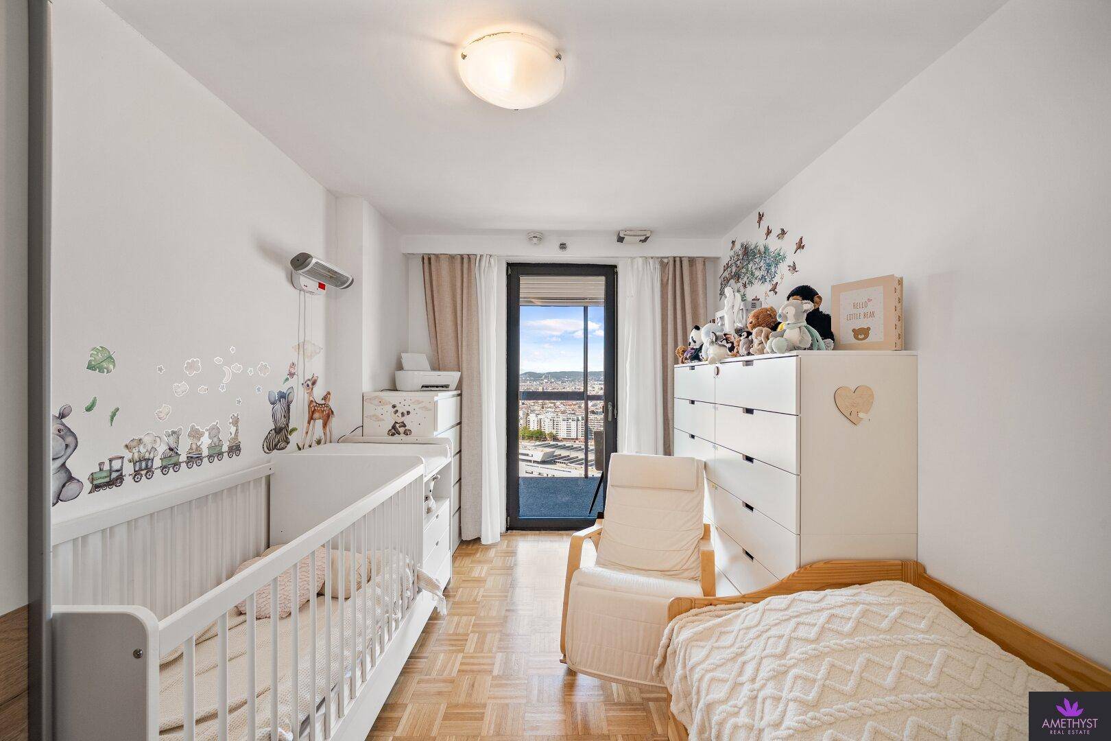 Helles Kinderzimmer mit Babybett, Wickelkommode und Zugang zu einem Balkon.