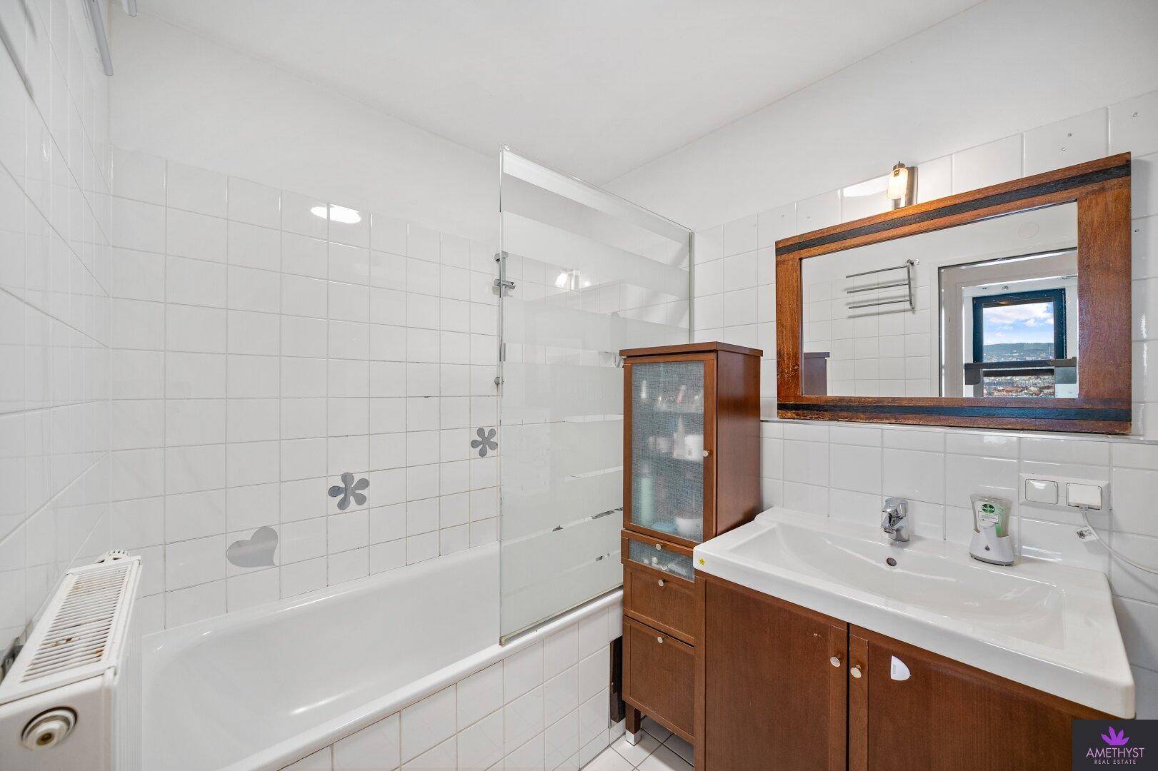 Badezimmer mit Badewanne, Waschbecken und weißen Fliesen, ausgestattet mit Holzmöbeln.