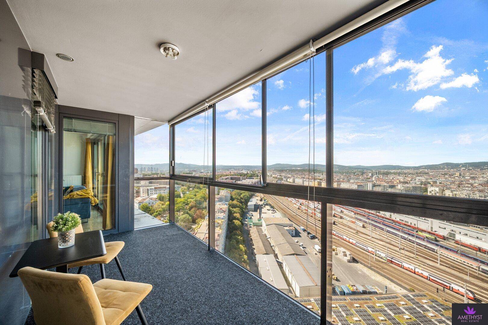 Verglaste Loggia mit Sitzgelegenheiten und weitem Blick über die Stadt und Bahnanlagen.