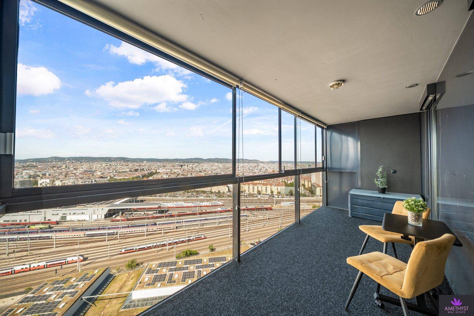 Verglaste Loggia mit weitem Blick über die Stadt und die darunterliegenden Bahnanlagen.