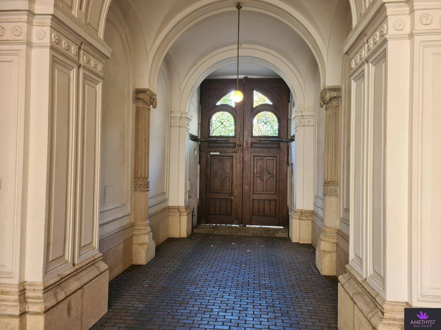 Repräsentativer Eingangsbereich mit hohen Bögen, Säulen und einer massiven Holztür in einem Altbau.
