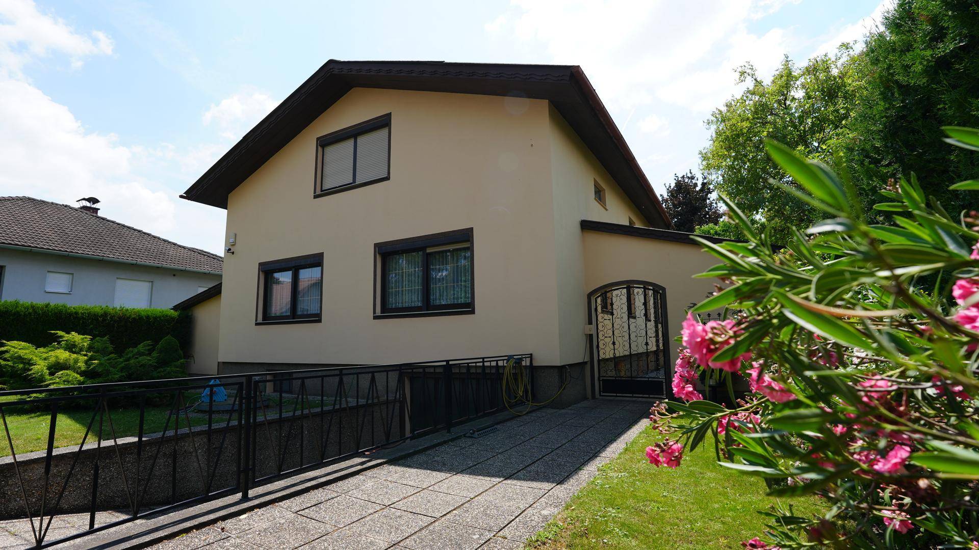 Einfamilienhaus mit beiger Fassade, Satteldach und einer praktischen Zufahrtsrampe im Vorgarten.