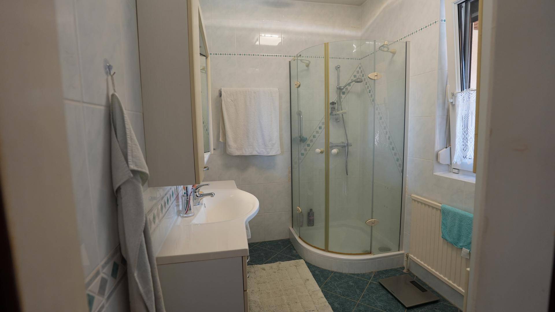 Helles Badezimmer mit Duschkabine, Waschbecken und Fenster für natürliche Belüftung.