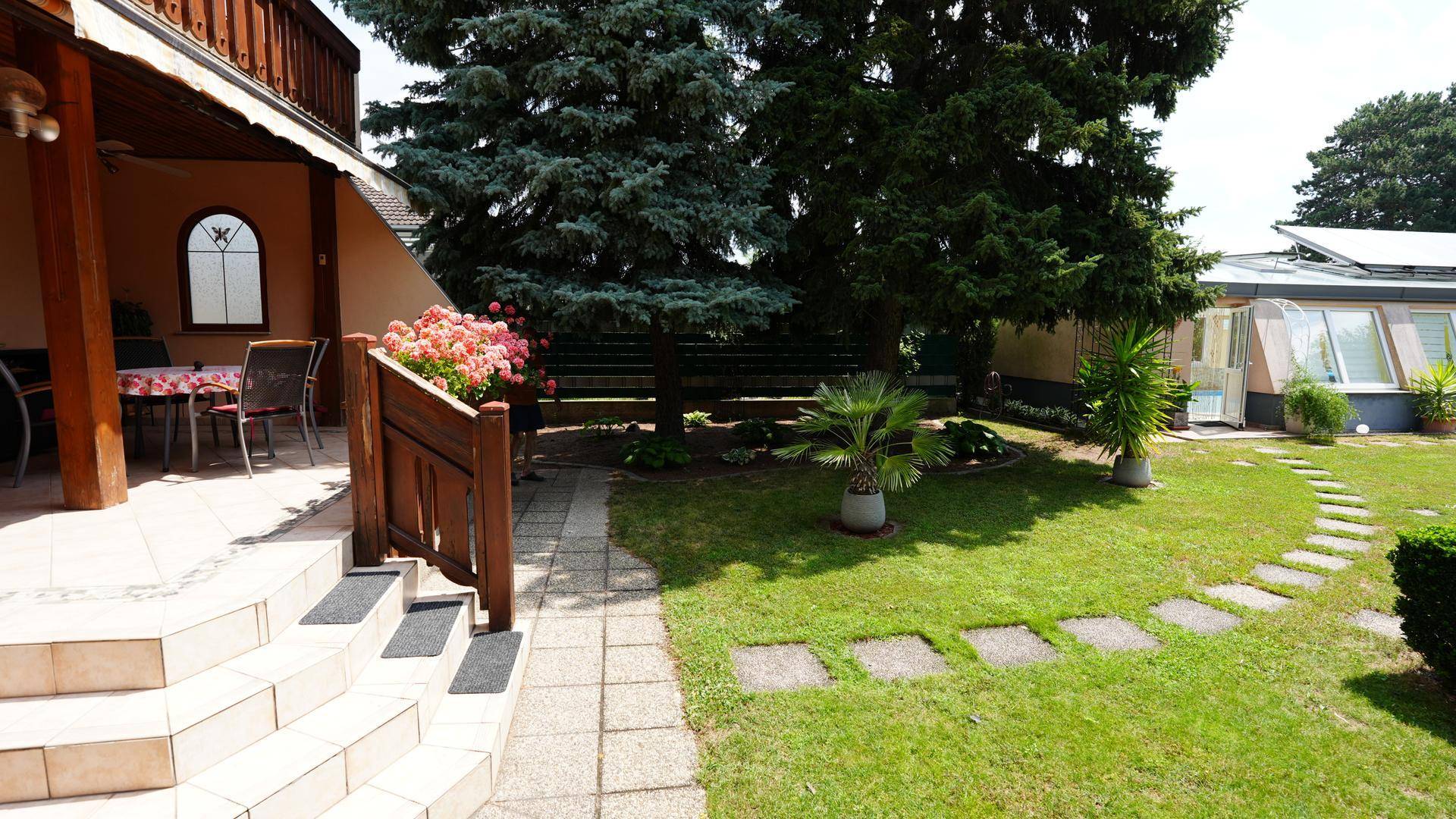 Gestufter Gartenbereich mit Treppe, Blumenbeeten und Blick auf die Terrasse des Hauptgebäudes.