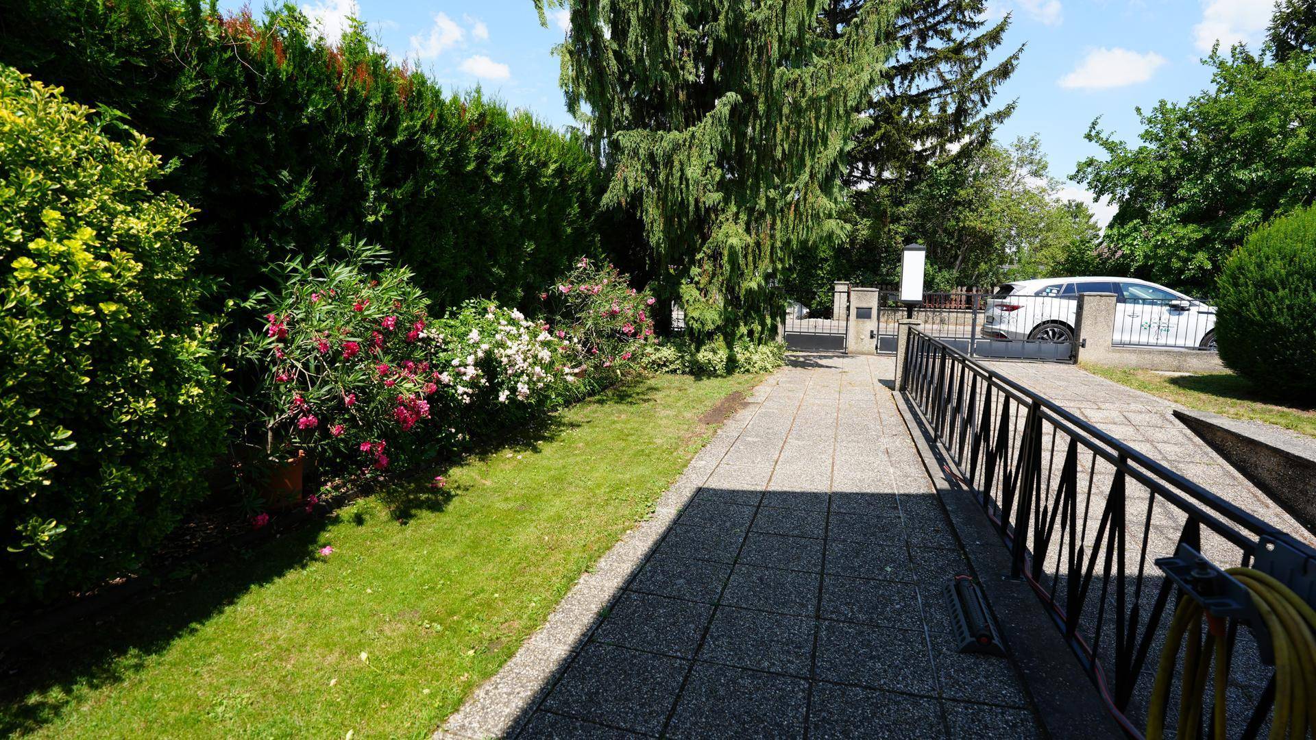 Gepflegter Vorgarten mit Rasenfläche, blühenden Blumenbeeten und einer barrierefreien Zufahrtsrampe.