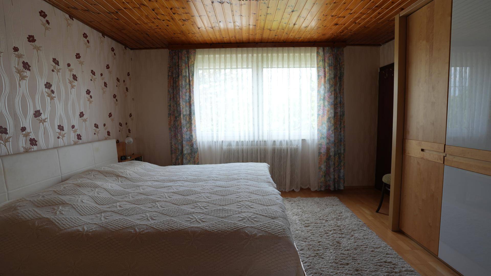 Gemütliches Schlafzimmer mit Doppelbett, Holzdecke und großem Fenster.