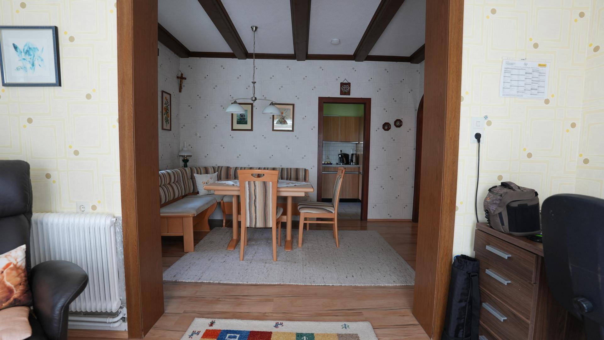 Rustikaler Essbereich mit Holzbalken an der Decke, Sitzbank und Blick in die Küche.
