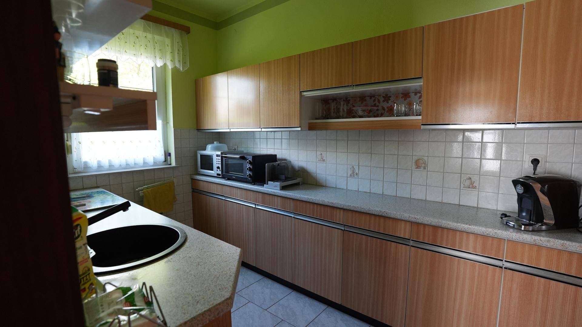 Funktionale Küche mit Holzschränken, grünen Wänden und einem Fenster für Tageslicht.
