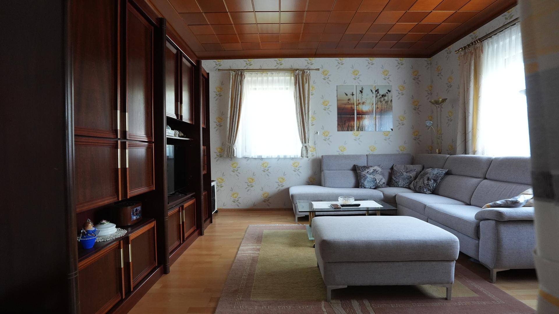 Gemütliches Wohnzimmer mit Holzdecke, großem Ecksofa und traditioneller Tapete.