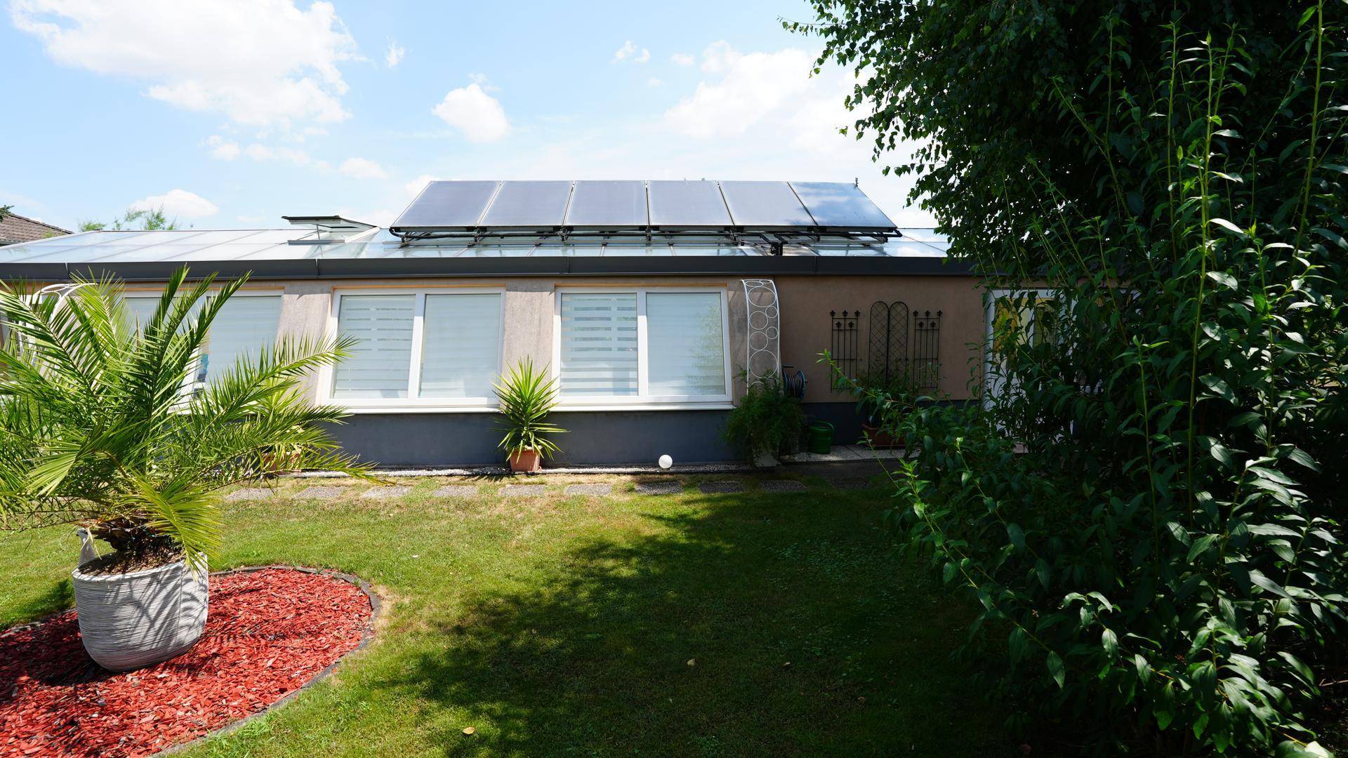 Rückseite des Gebäudes mit Photovoltaikanlage auf dem Dach und einem gepflegten Gartenbereich.