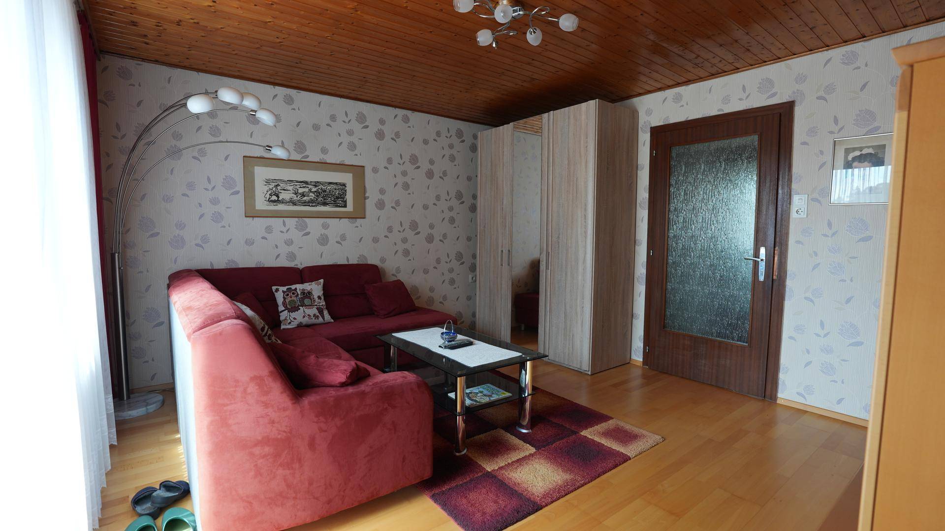 Helles Schlafzimmer mit rotem Sofa, Holzdecke und gemusterter Tapete.